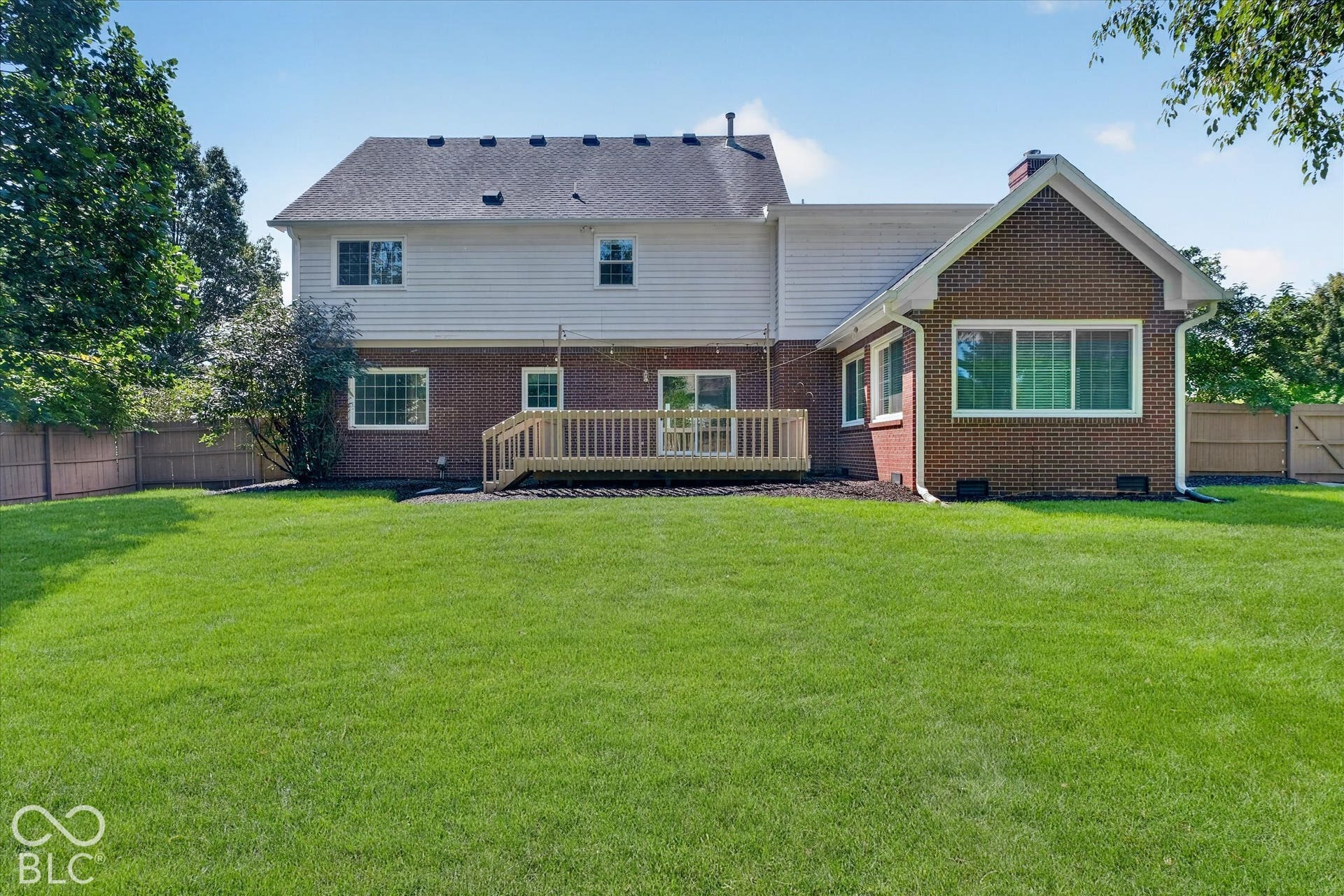 Expansive green lawn with a wood fence, brick and siding exterior, multi-pane windows, and a wood deck