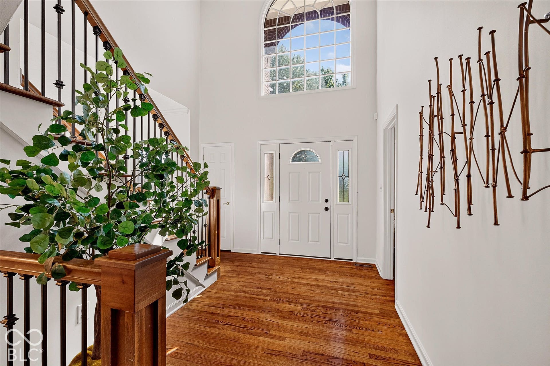 Hardwood flooring, two-story entryway, architectural arched window, white entry door with sidelights, and a staircase featuring wood newels and wrought iron balusters