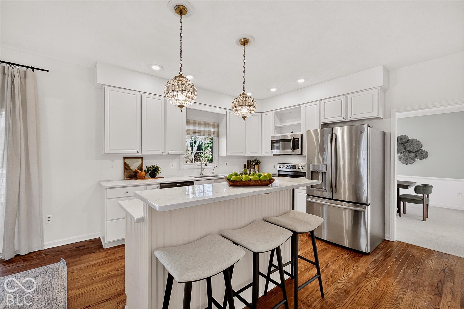 Kitchen featuring white shaker cabinetry, stainless steel appliances, a center island with countertop seating, wood-finish flooring, and two pendant light fixtures