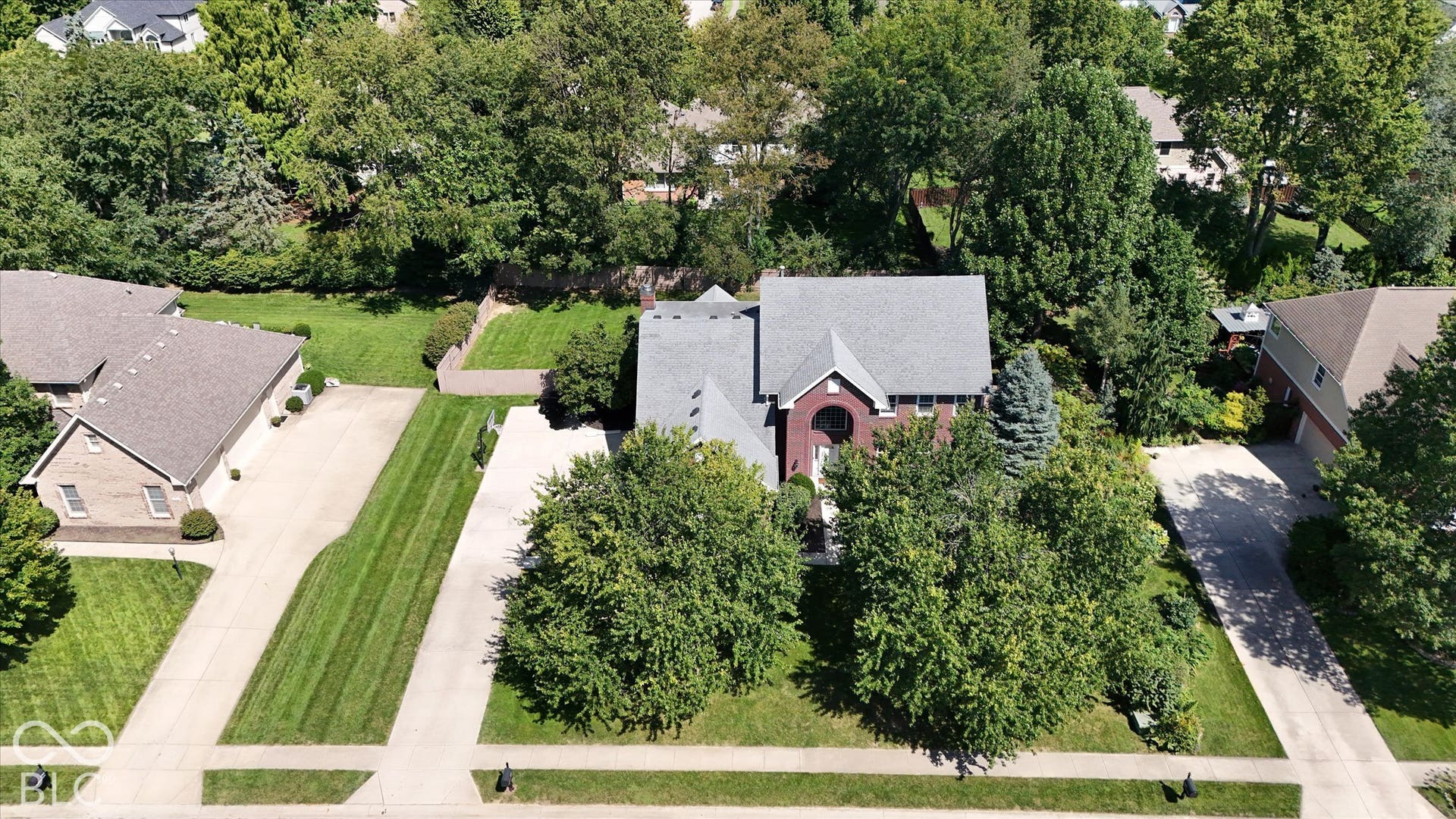 Brick exterior residence with a shingled roof, mature trees, and a concrete driveway