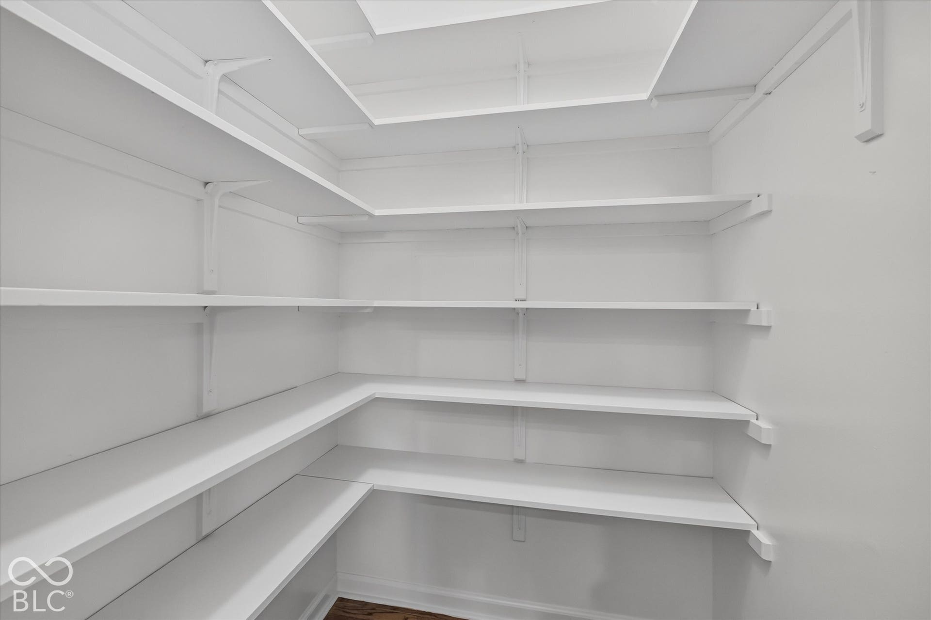 Expansive walk-in pantry with white shelving, L-shaped configurations, multiple levels of storage, and wood-finish flooring