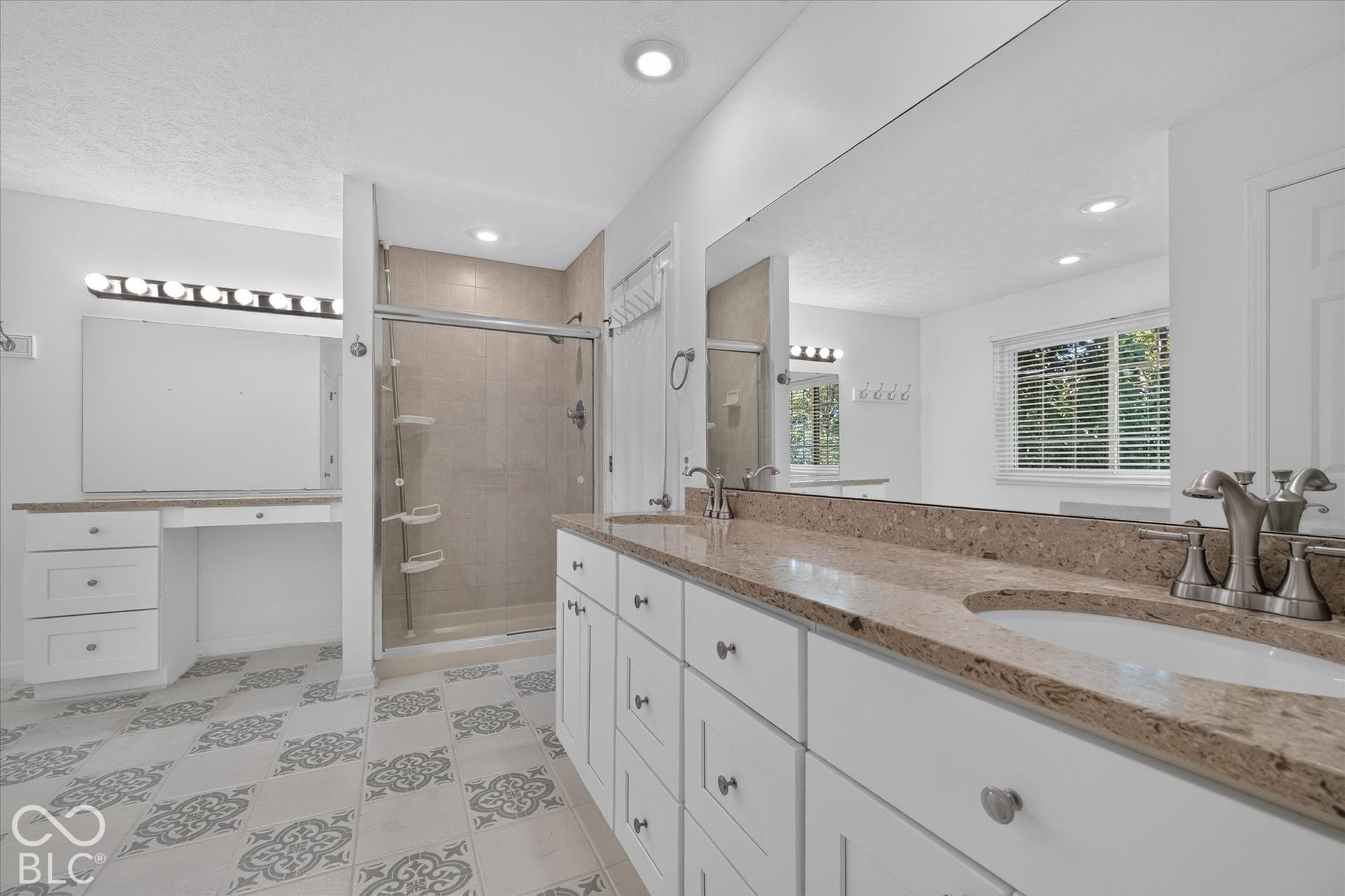 Bathroom featuring patterned floor tiles, a glass-enclosed shower, dual vanity with undermount sinks, and a built-in makeup vanity