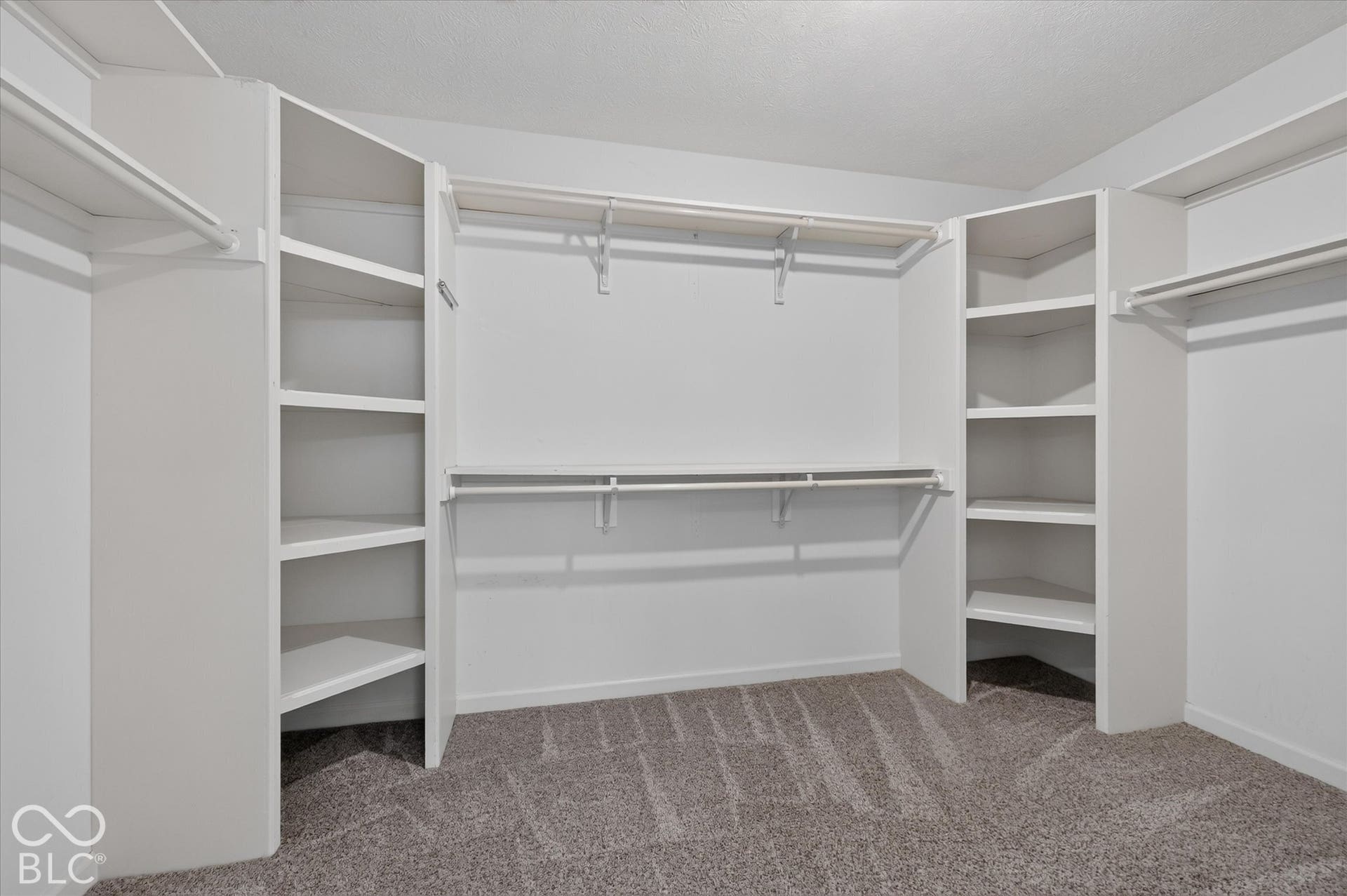 Built-in shelving, multiple hanging rods, and neutral carpeting