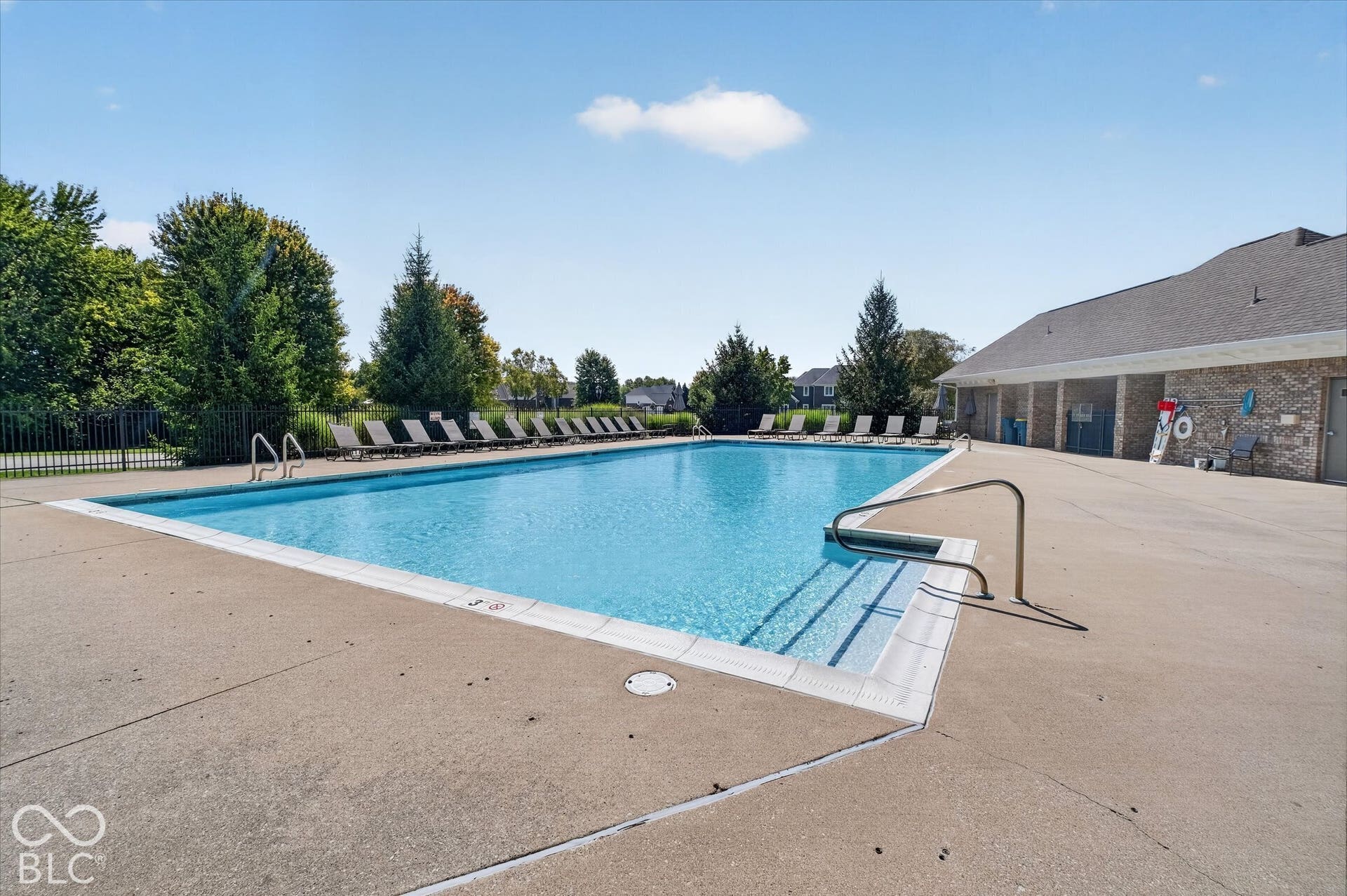 Outdoor swimming pool with concrete decking, surrounding perimeter fence, and adjacent brick-clad building