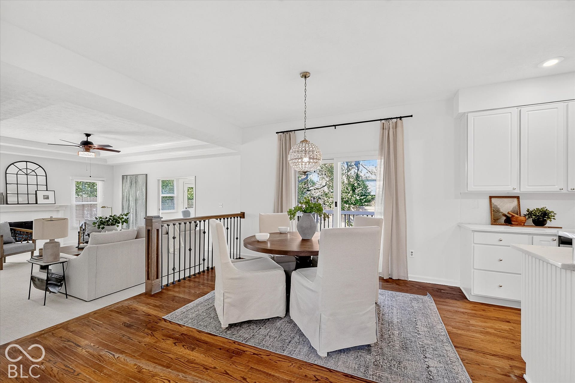 Hardwood flooring, white kitchen cabinetry, sliding glass door, decorative lighting fixture, and a white fireplace