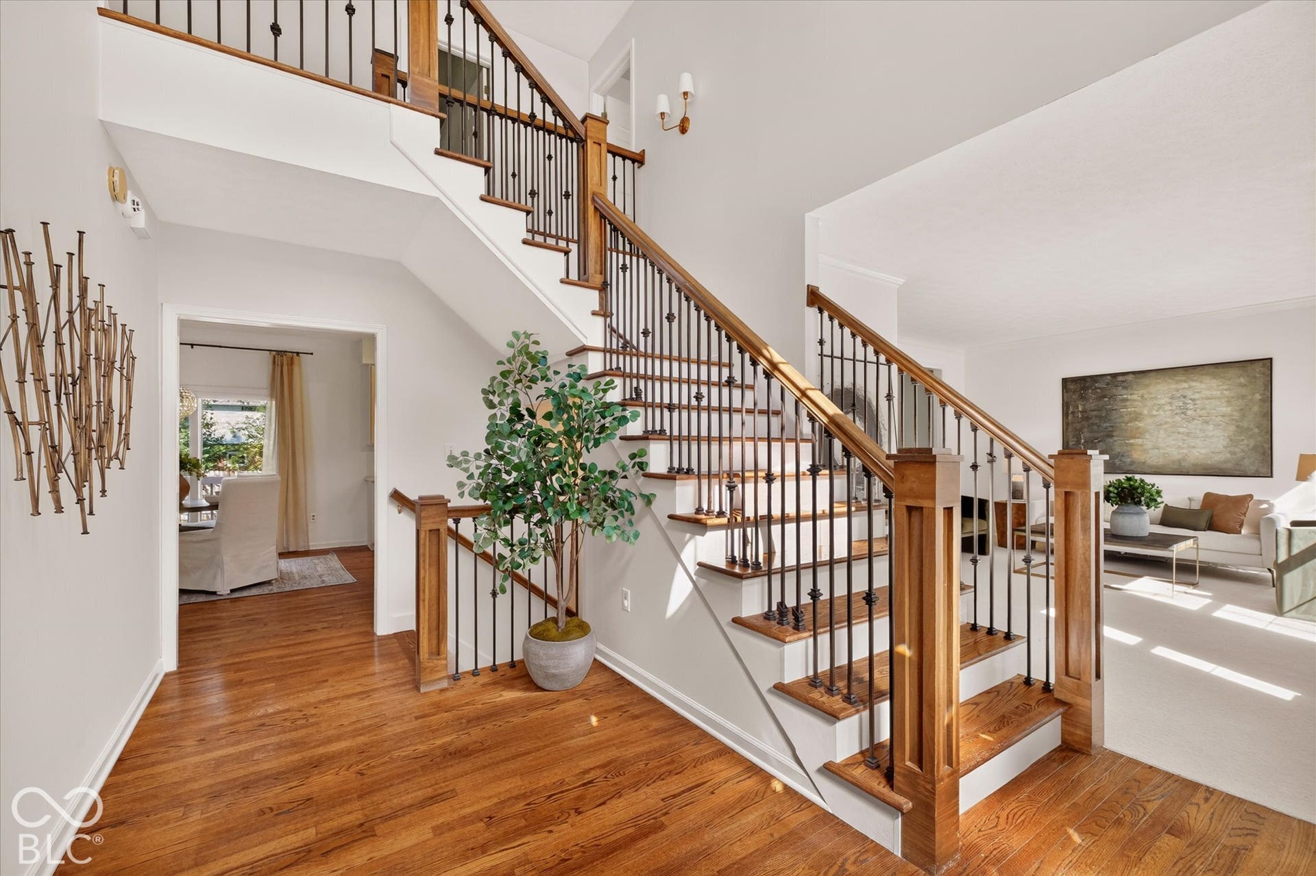 Hardwood flooring, custom staircase with wrought iron balusters and wood handrail, recessed wall niche, and bright interior lighting