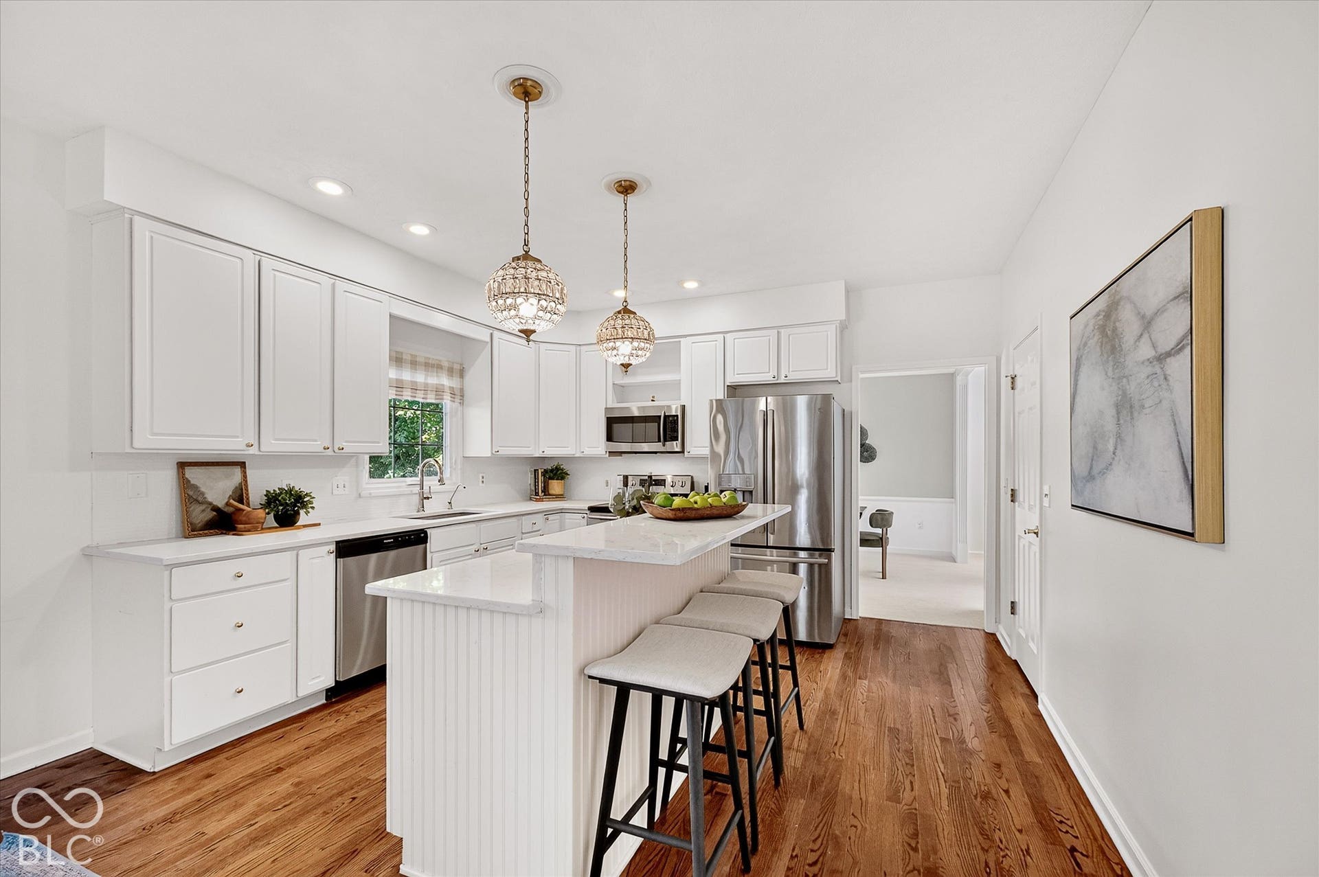 White cabinetry, stainless steel appliances, wood-finish flooring, island seating, and recessed lighting
