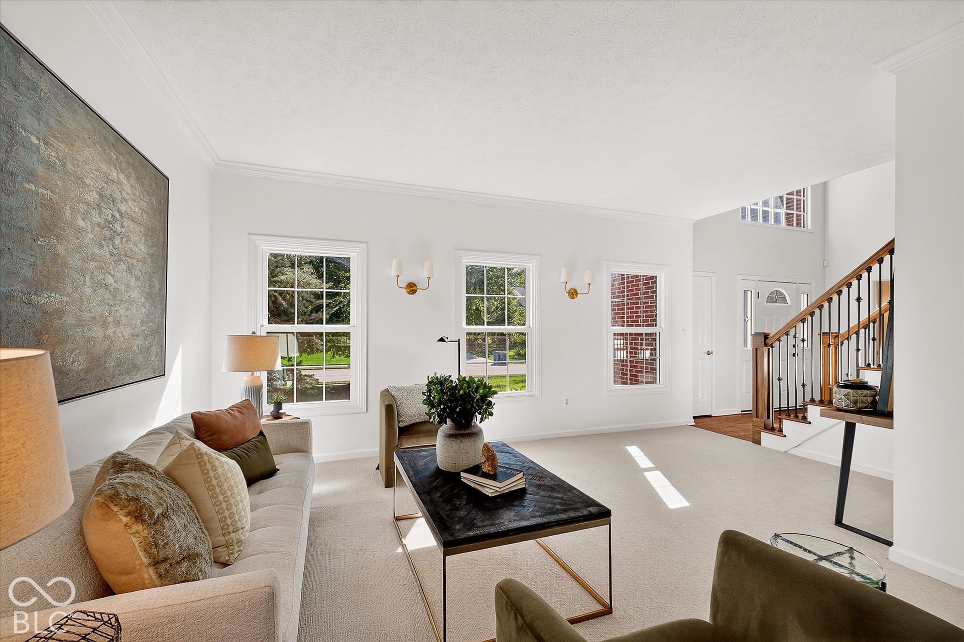 White-painted walls and trim with crown molding, double-hung windows, a staircase with wood-finish handrail and black metal balusters, and a front entry door with an arched transom window