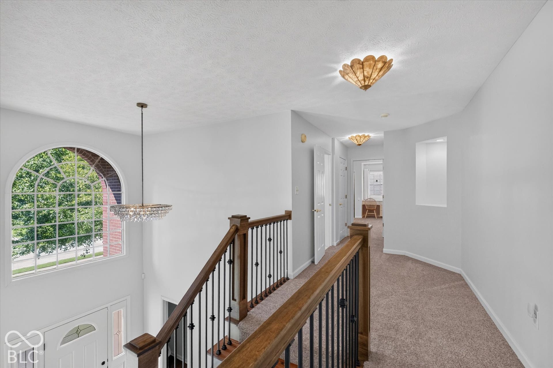 Arched window, crystal chandelier, hardwood handrail, wrought iron balusters, and recessed wall niche