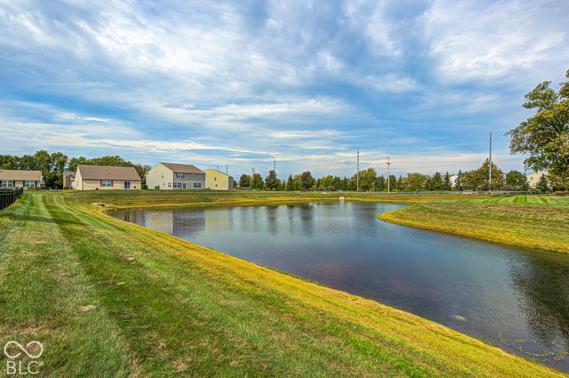 Serene waterfront setting with expansive manicured lawn, mature landscaping, and calm water feature