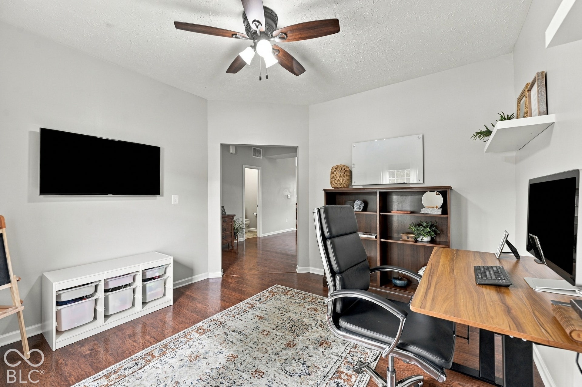 Wood-finish flooring, built-in shelving, ceiling fan with integrated lighting, and neutral wall tones