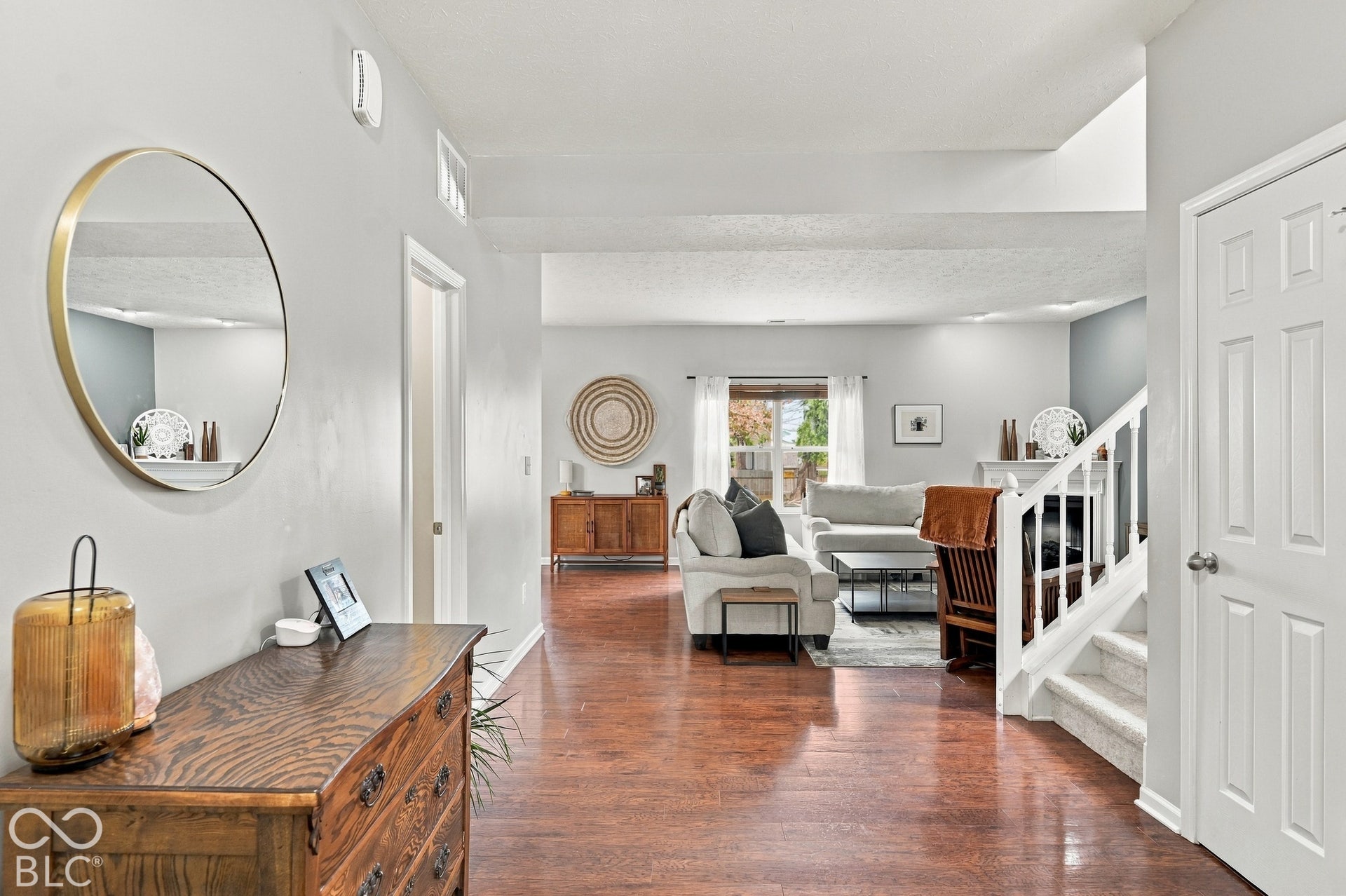 Bright foyer featuring a circular brass-framed mirror, hardwood flooring throughout, and an open floor plan with sight lines into the living areas