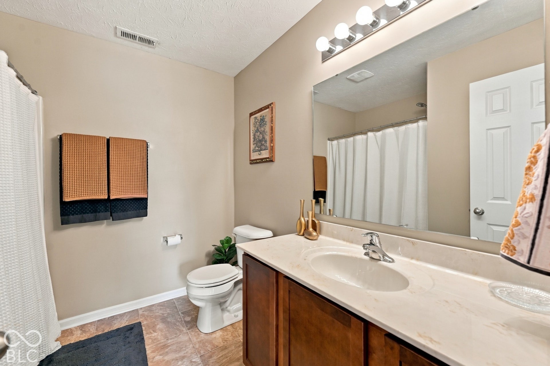 Bathroom featuring a wood-finish vanity, light-toned countertop, integrated sink, and an expansive mirror