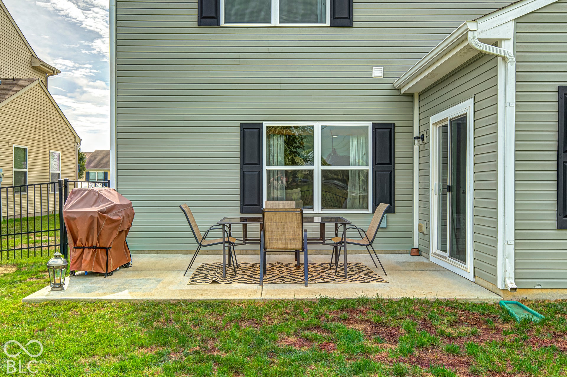 Rear exterior featuring siding, a concrete patio, sliding glass door, and a black wrought iron fence
