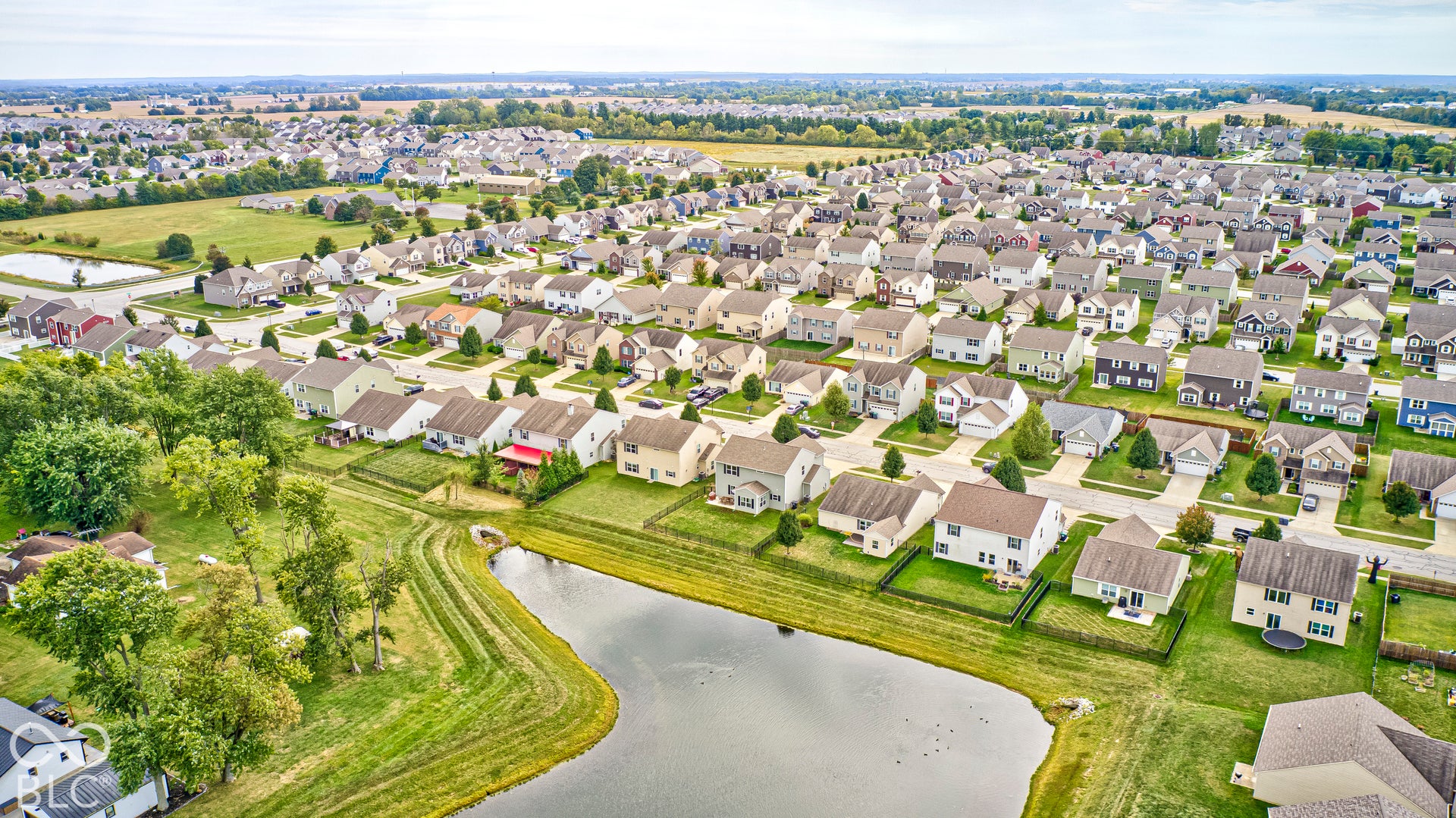 Expansive residential development with numerous single-family homes, featuring a prominent pond and surrounding green spaces