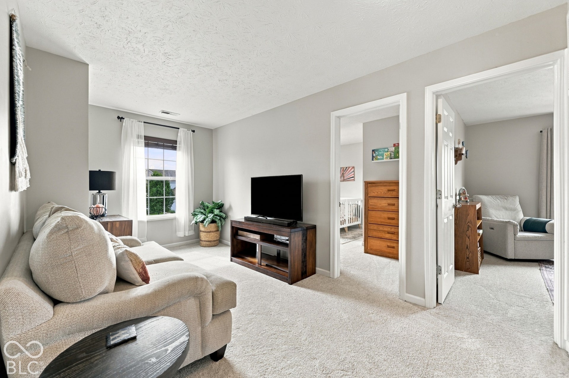 Carpeted room featuring light gray walls, a window with white curtains, and two open doorways