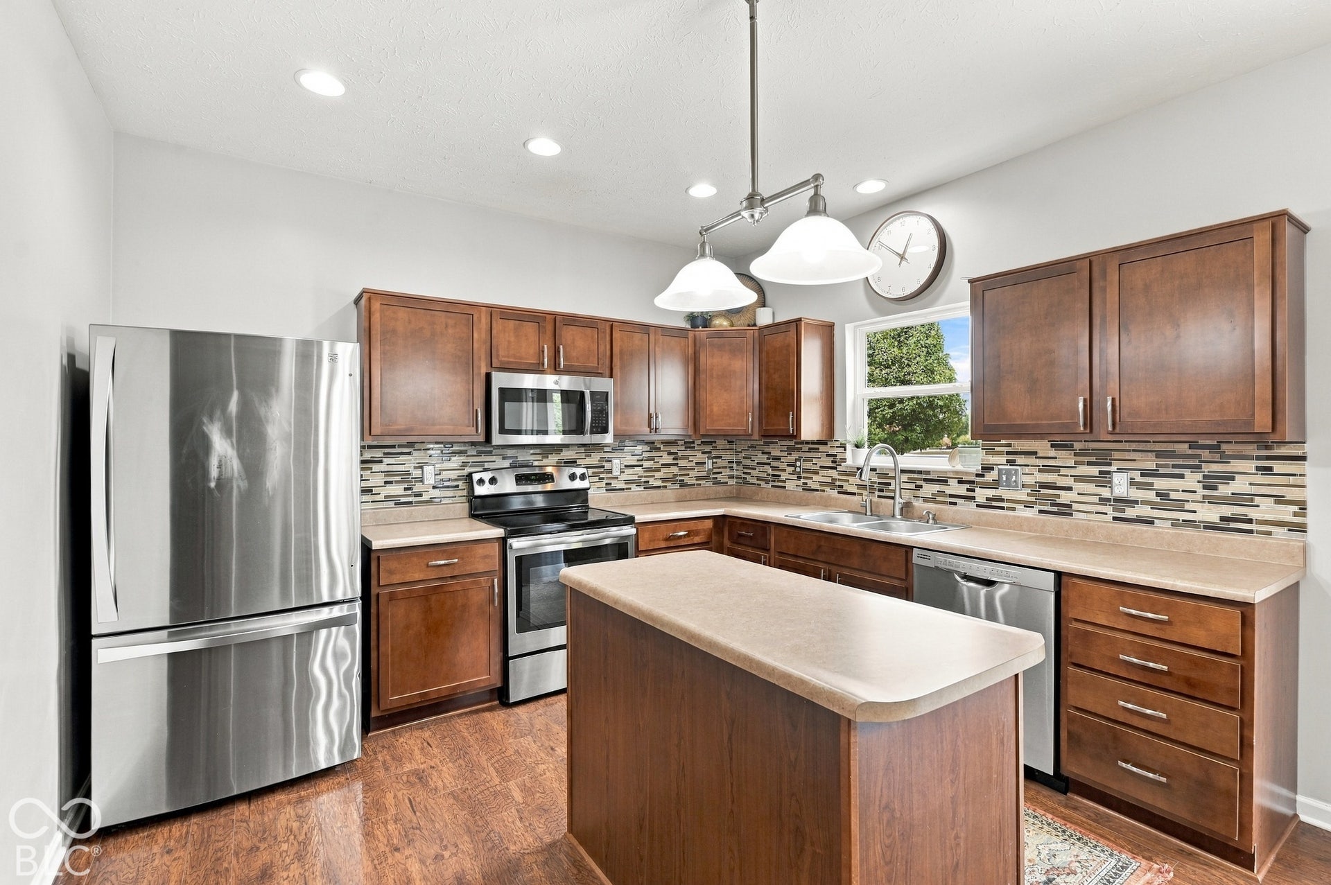 Kitchen featuring wood-finish flooring, stainless steel appliances, wood cabinetry, a tile backsplash, and an island with a countertop