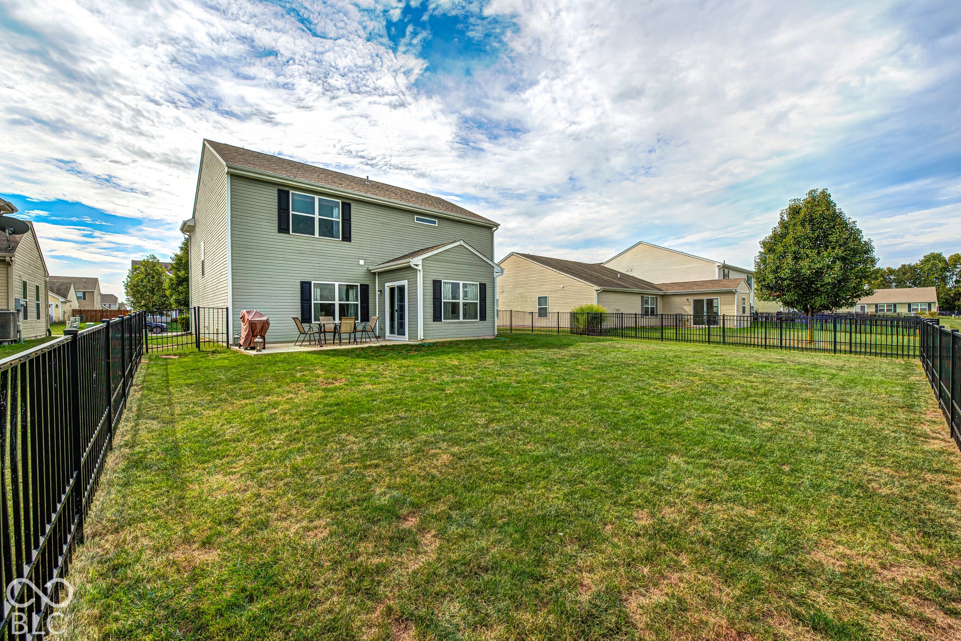 Expansive green lawn with complete black metal fencing, featuring a concrete patio and a rear house exterior with multiple windows