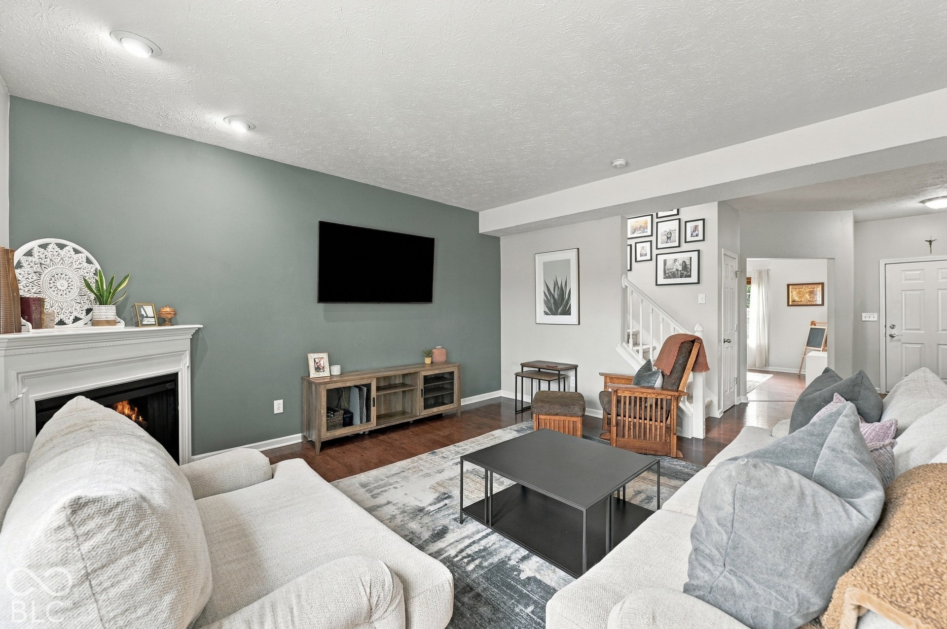 Living area featuring a fireplace with a white mantel, recessed lighting, wood-finish flooring, and a staircase with white balusters