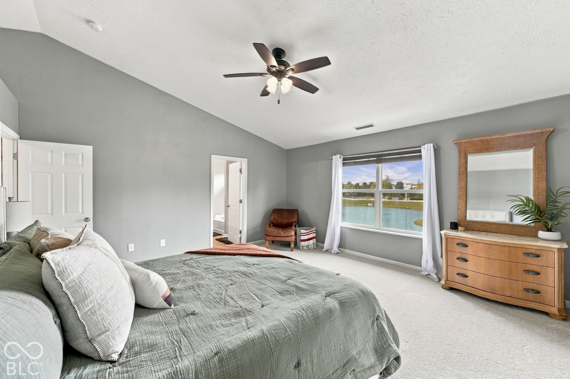 Vaulted ceiling with a ceiling fan, carpeted flooring, and a window overlooking a water feature