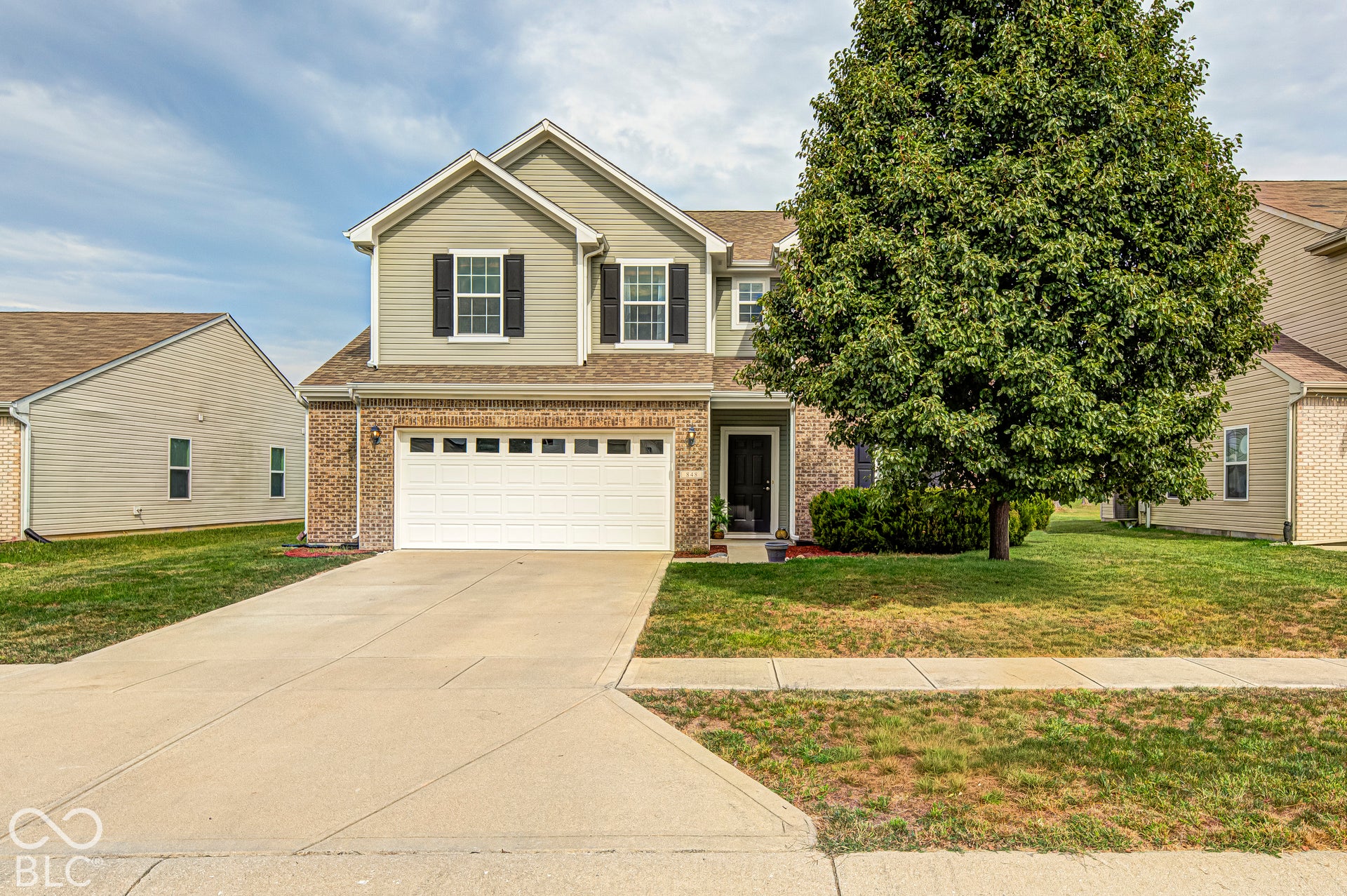 Two-story residence featuring a brick and siding exterior, an attached two-car garage, a concrete driveway, a front entry, and a mature tree
