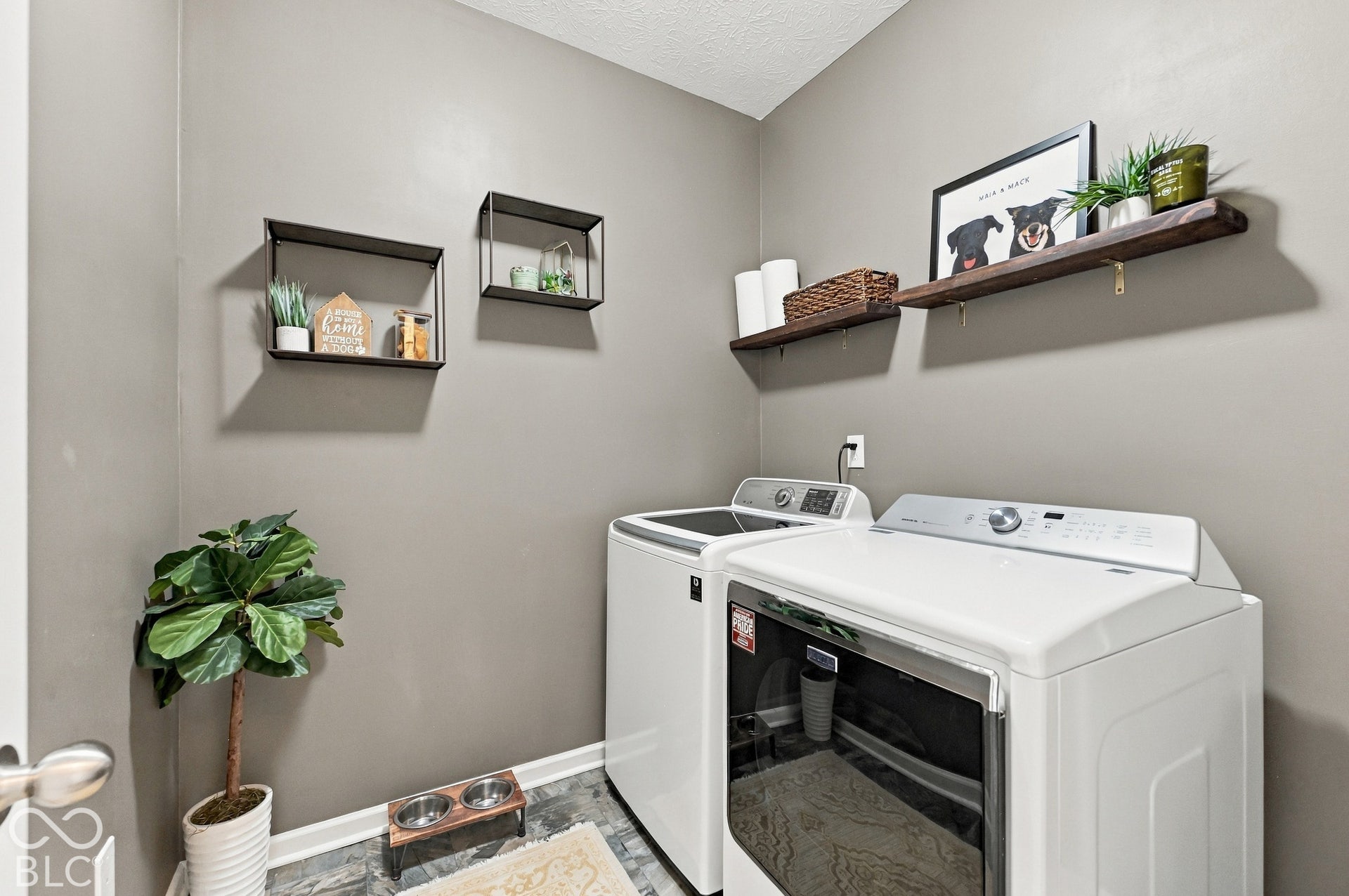 Laundry area featuring wood-finish flooring, two wall-mounted floating shelves, and two wall-mounted rectangular metal shelves
