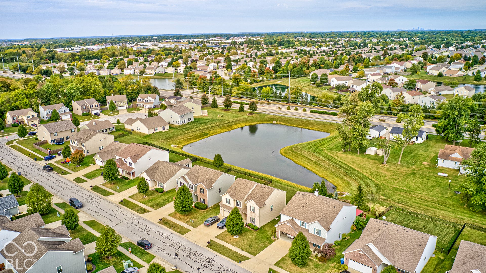 Aerial view of this suburban community featuring tree-lined streets, manicured lawns, and a scenic retention pond with landscaped grounds
