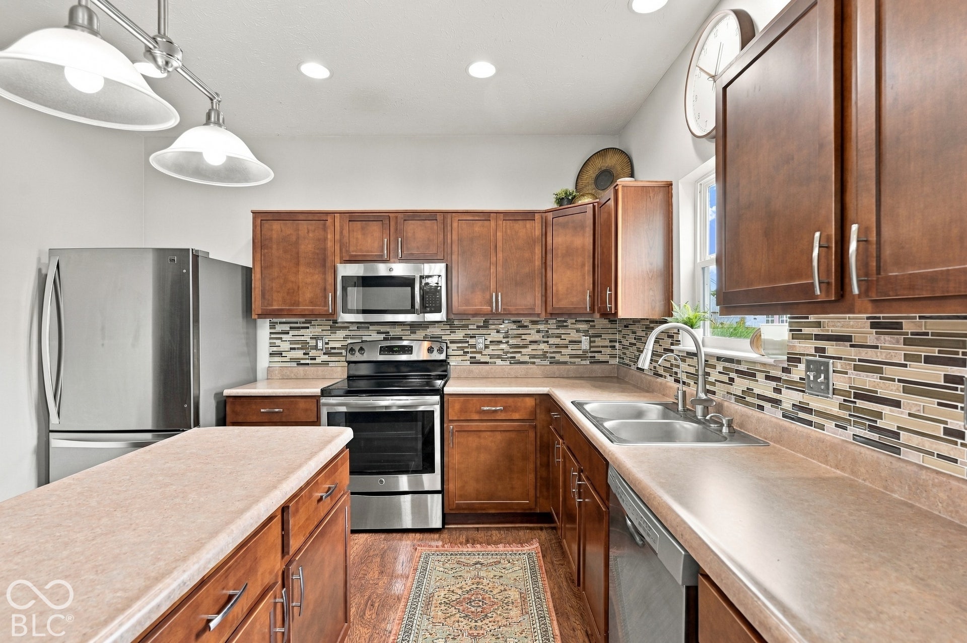 Stainless steel appliances, wood-finish cabinetry, tile backsplash, double basin sink, and recessed lighting