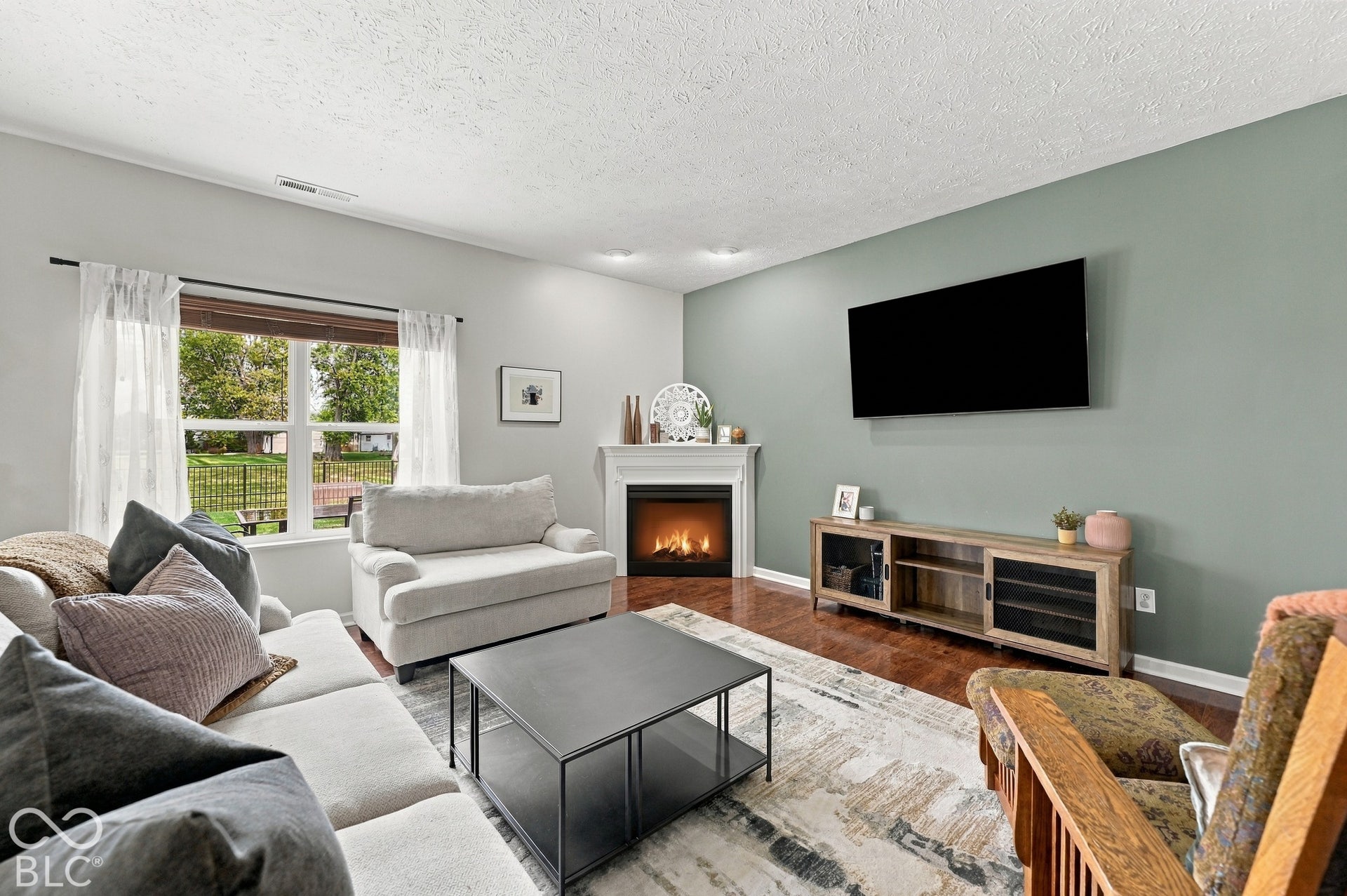 Hardwood-style flooring, a white mantel fireplace, and a light green accent wall define this living space