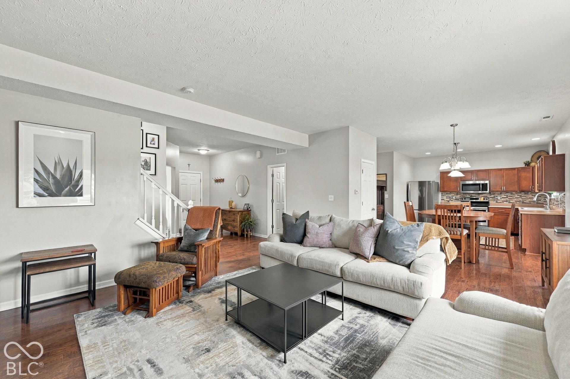 Open-concept living space featuring wood-finish flooring, a contemporary staircase with white railings, and recessed lighting