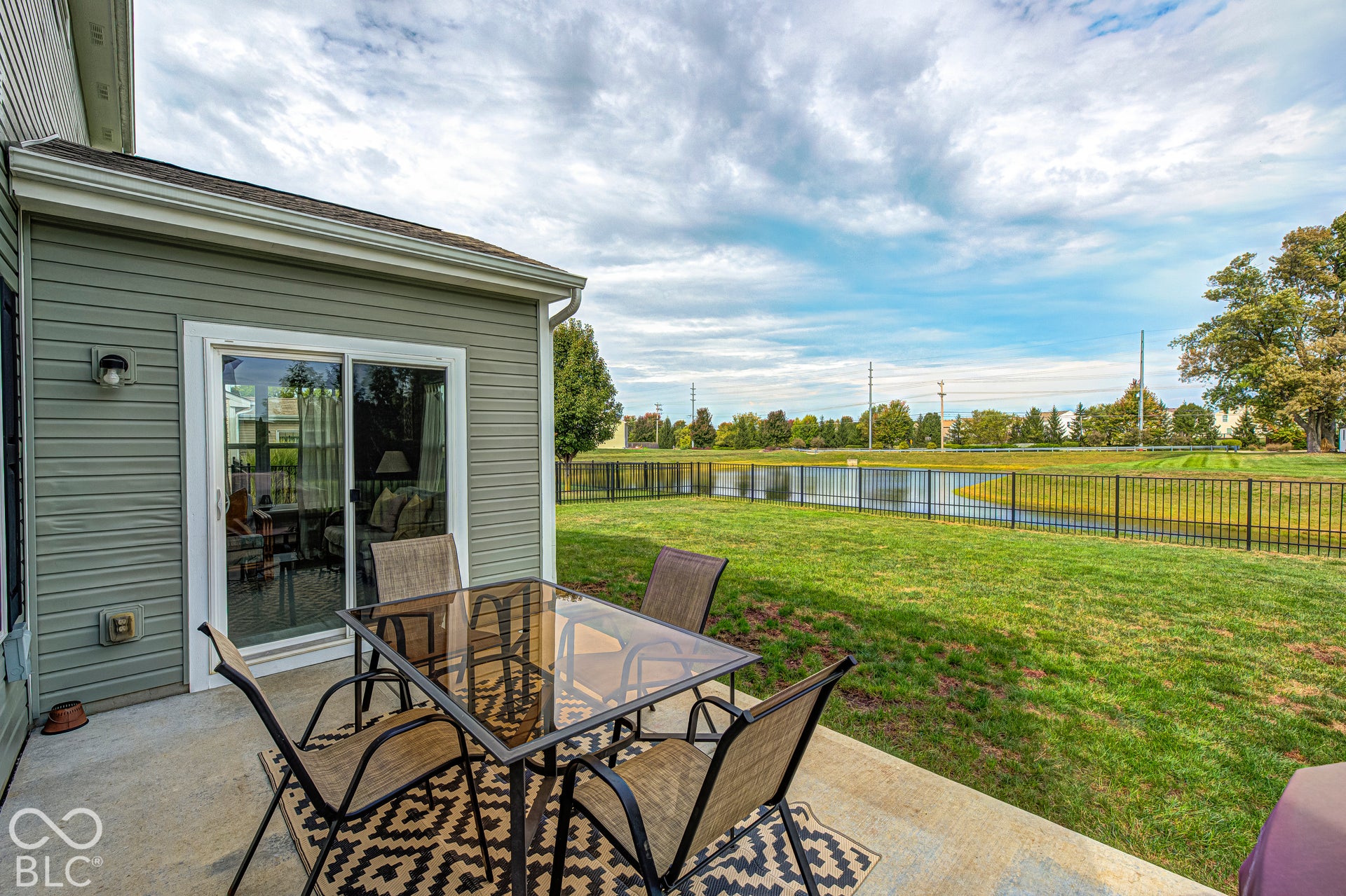 Concrete patio with direct access to a grassy area, a pond, and a black metal fence