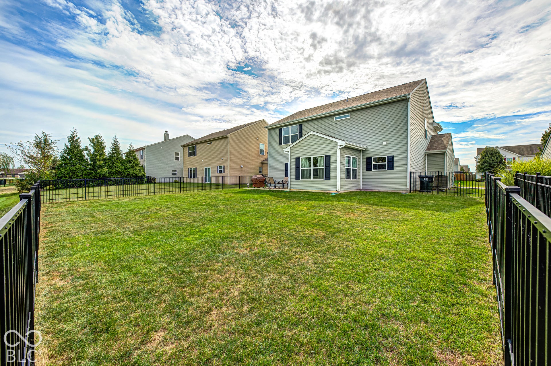 Expansive fenced backyard featuring a manicured lawn, established landscaping, and a bay window on the home's exterior