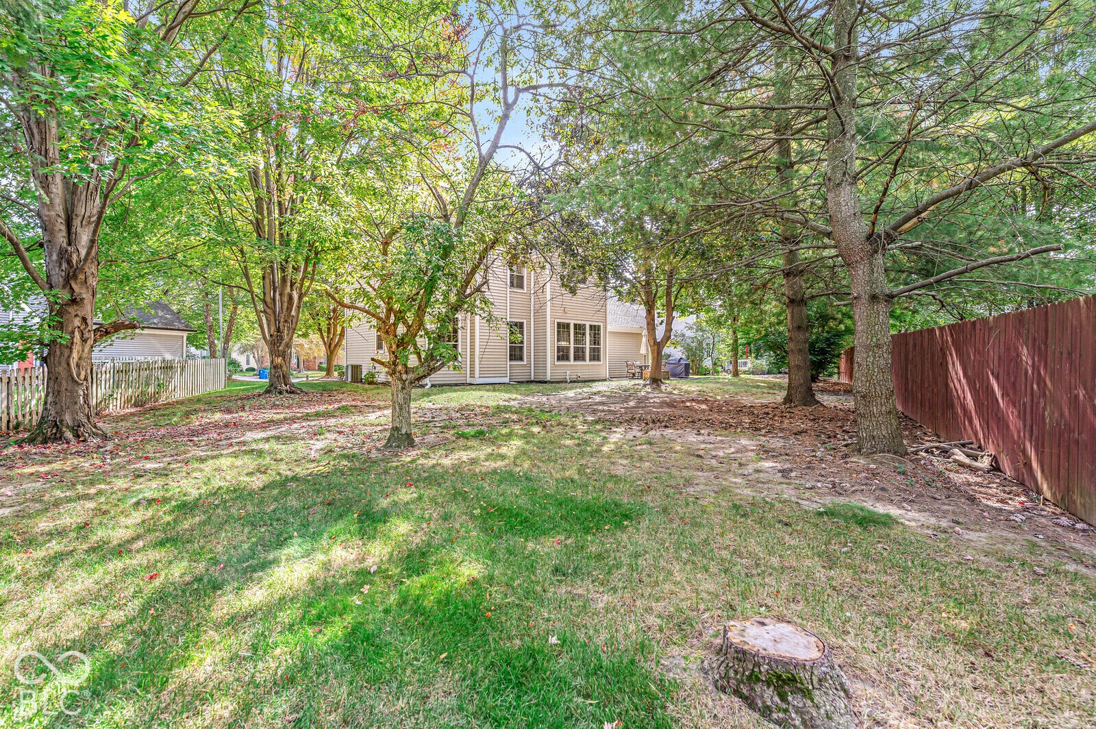 Expansive backyard featuring mature trees, a wooden privacy fence, and a two-story residence with multiple window installations