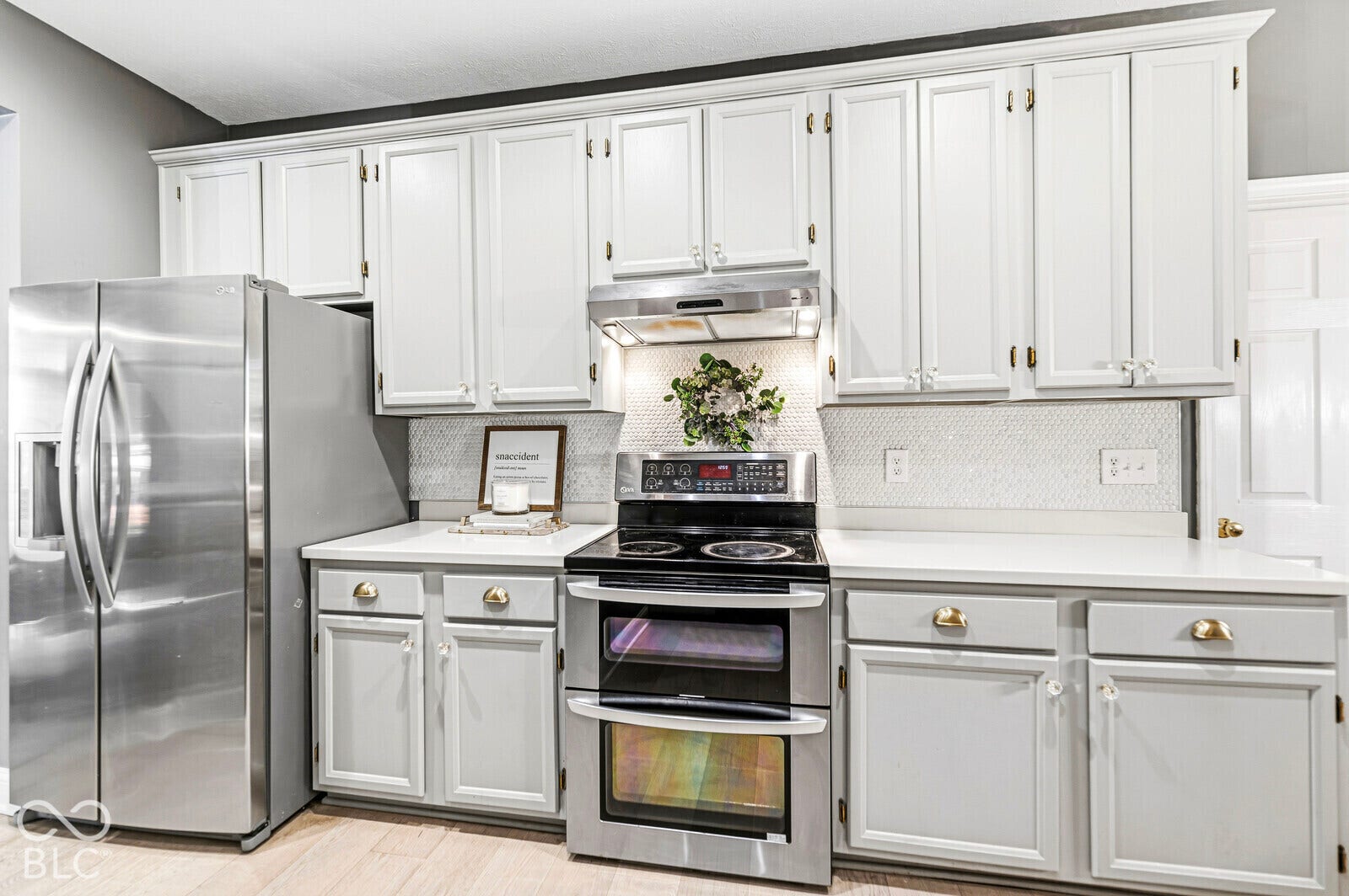 Stainless steel side-by-side refrigerator, stainless steel electric range with double oven, white shaker-style cabinetry, white countertops, and geometric pattern backsplash