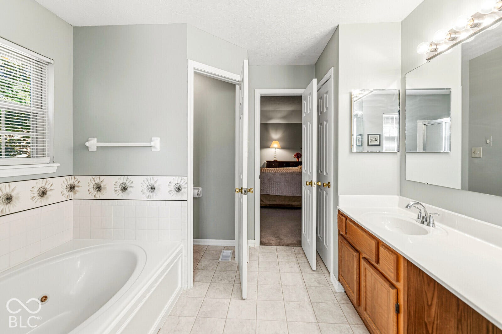 Built-in soaking tub, vanity with integrated sink, large wall-mounted mirror, and tile flooring