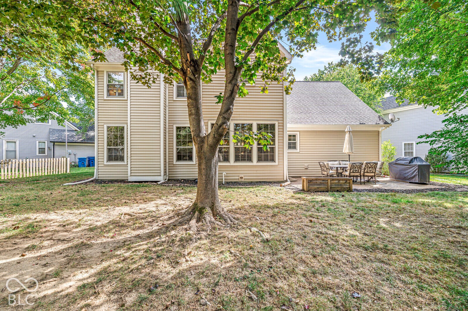 Expansive rear yard featuring mature trees, a paver patio, and light-colored siding