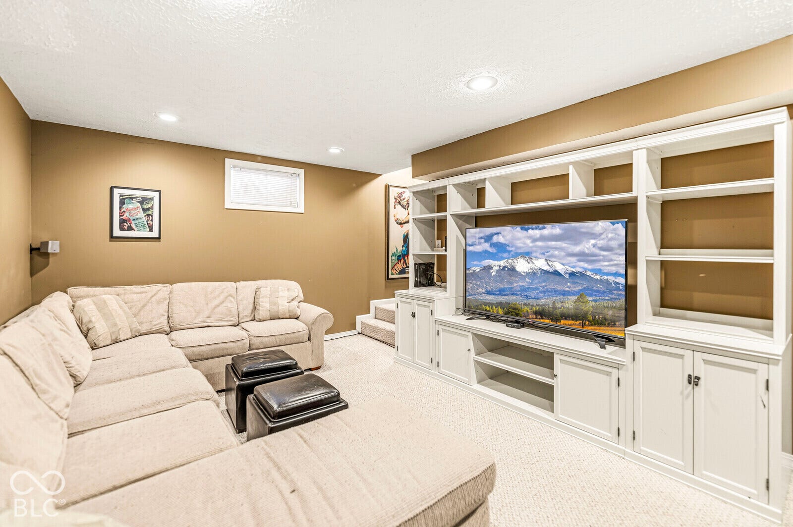 Recessed lighting illuminates the space, featuring a built-in media center with open shelving and cabinet storage, and a carpeted floor