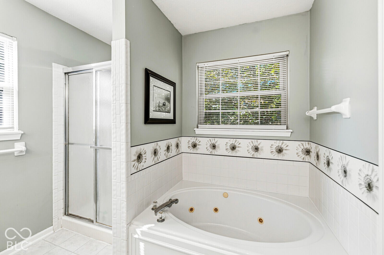 Corner jetted tub with tile surround, separate shower with sliding door, and a window with blinds