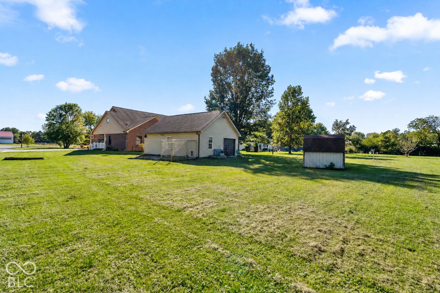 Expansive grassy yard area featuring a detached shed and mature trees