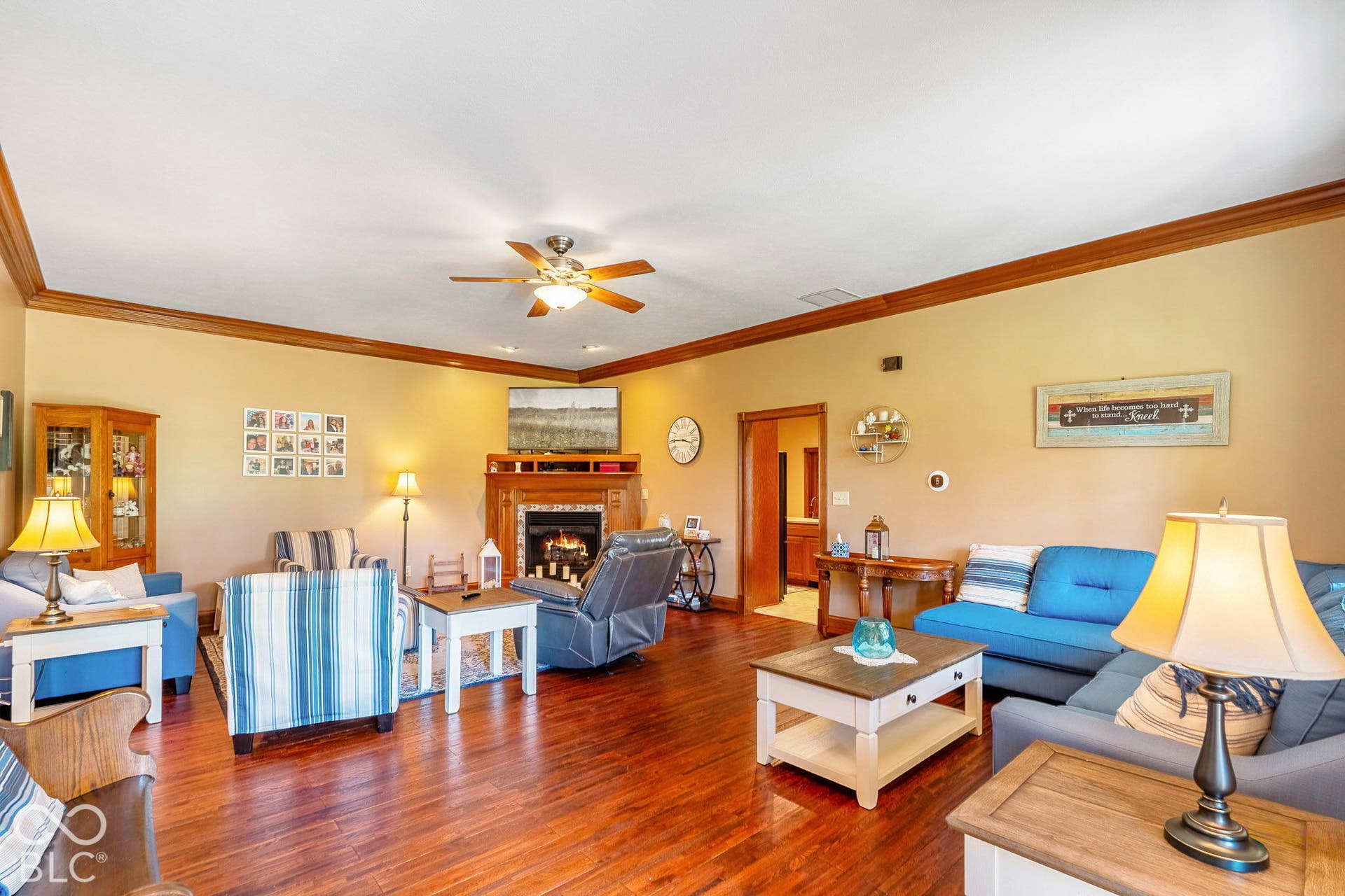 Spacious living area featuring wood-finish flooring, a ceiling fan, crown molding, and a built-in fireplace with a wood mantle