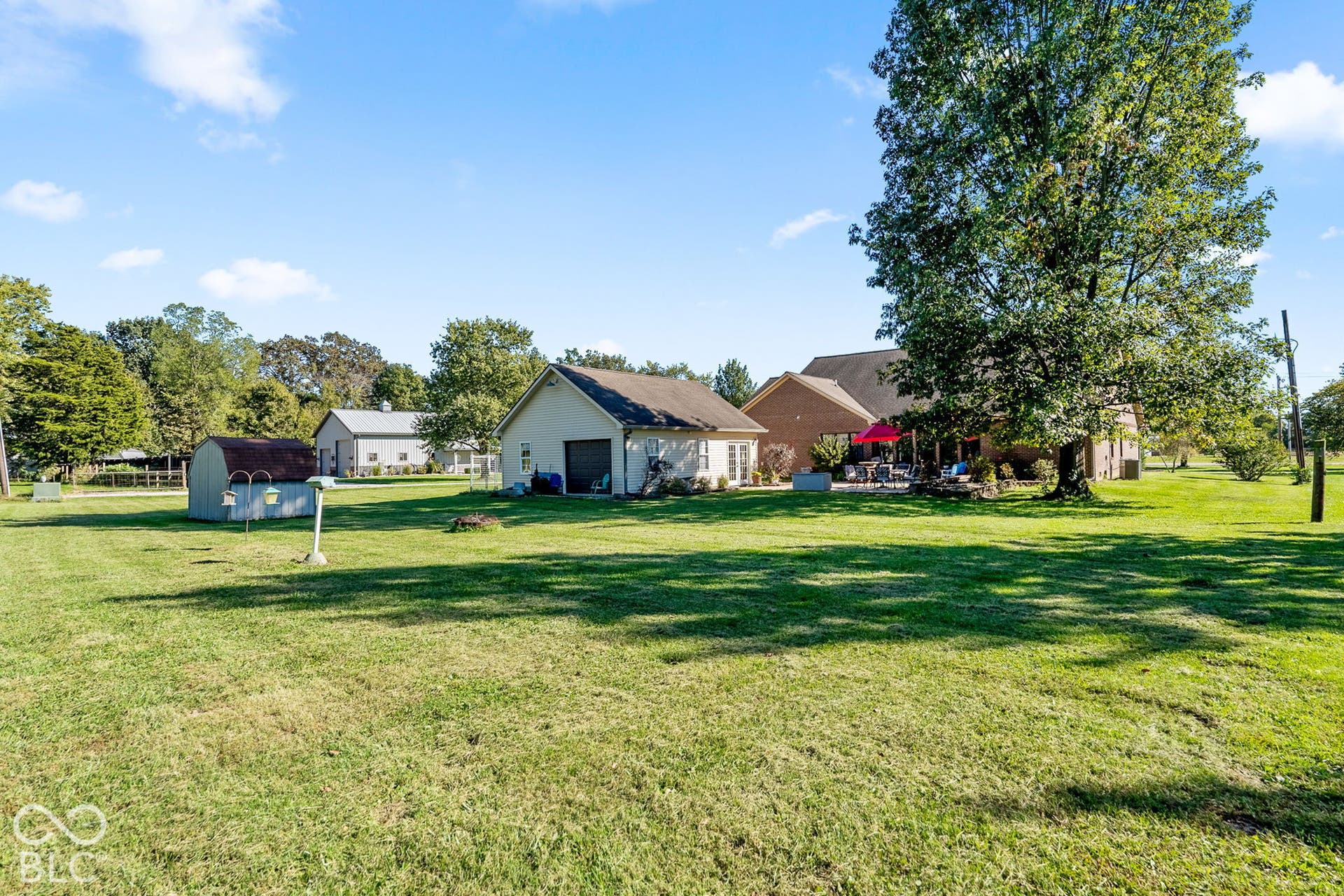Expansive grass lawn with mature trees, detached garage, and additional outbuilding