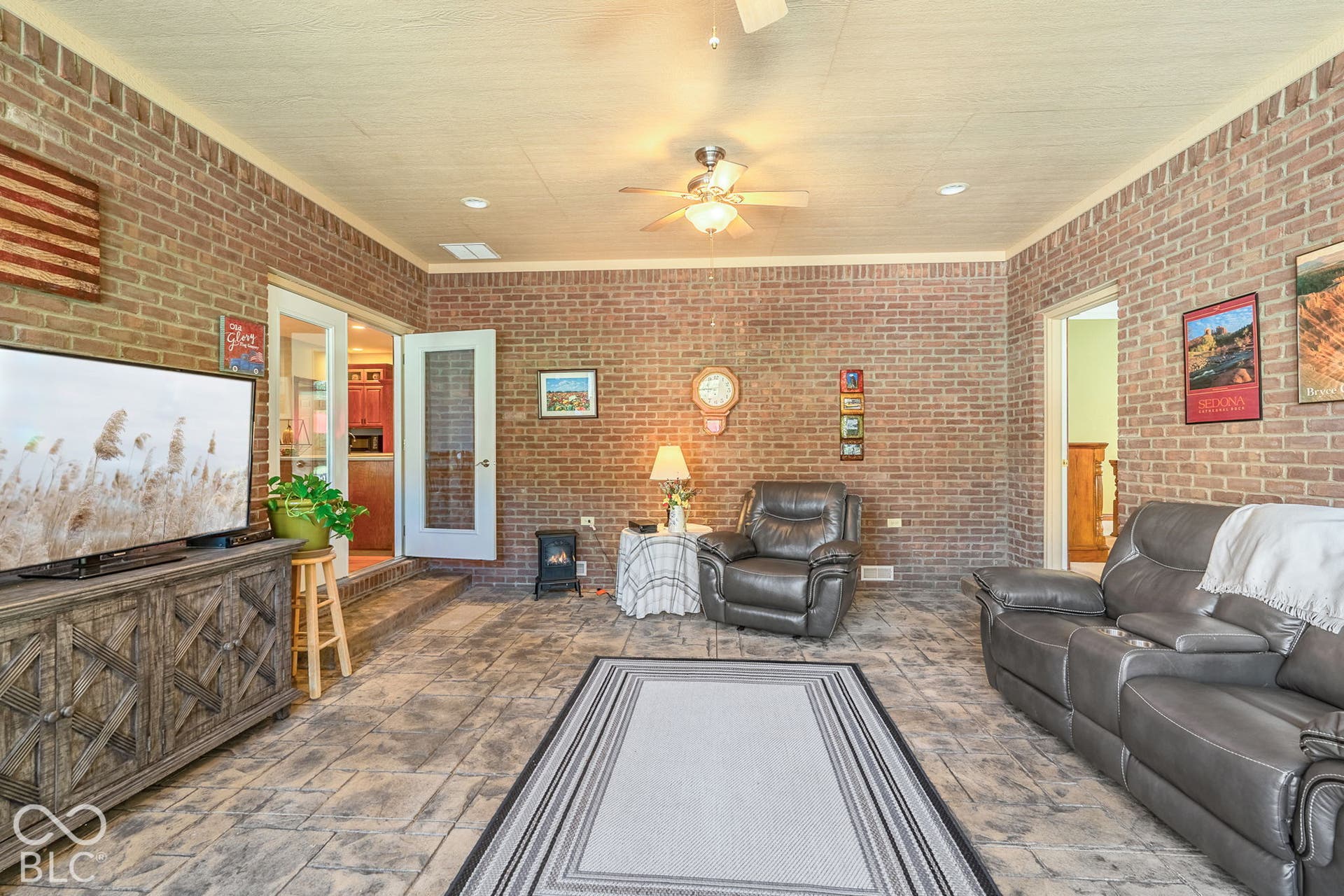 Exposed brick walls, stamped concrete flooring, ceiling fan, recessed lighting, and double glass-paneled doors