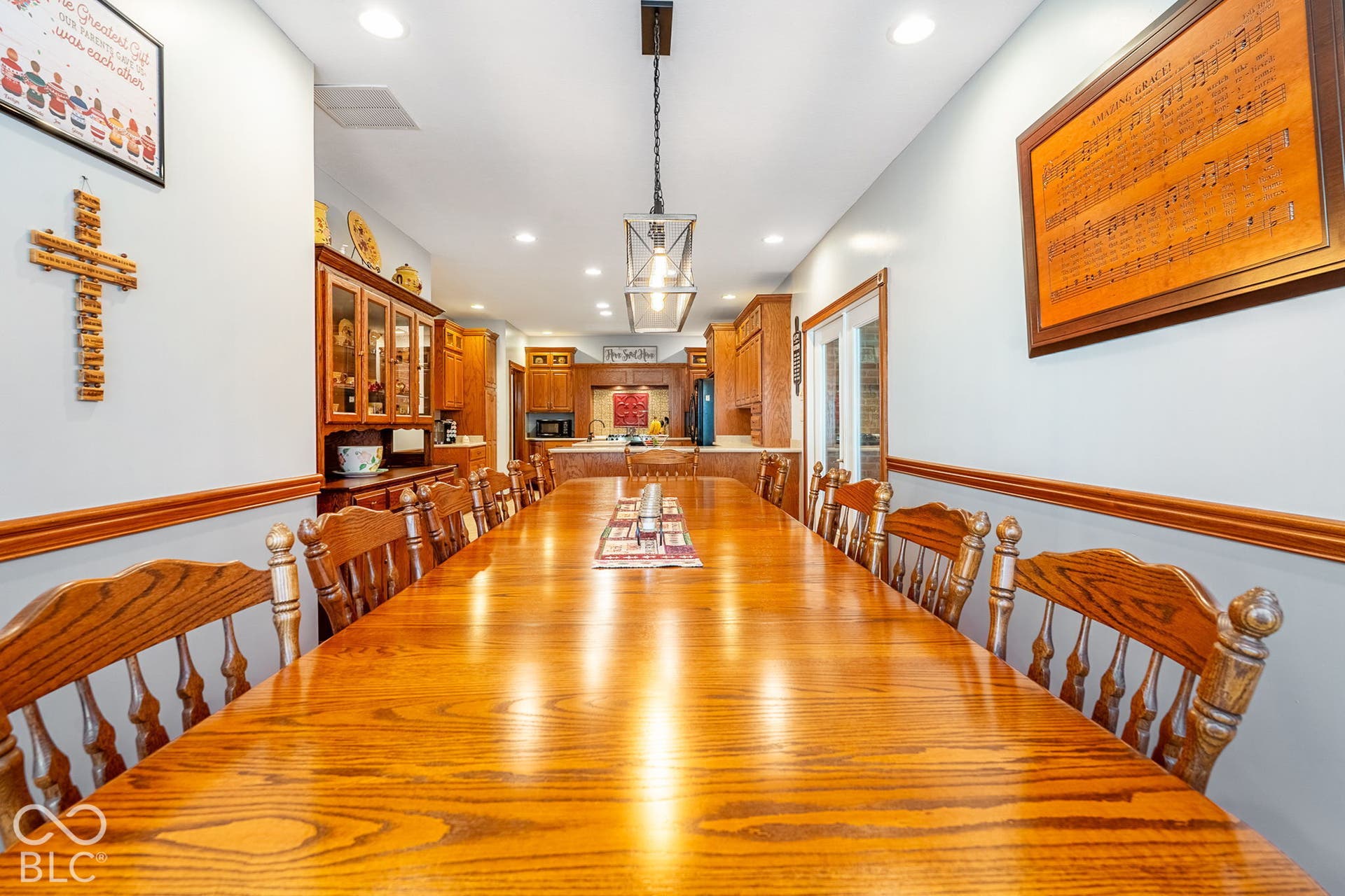 Expansive dining area featuring a lengthy wood-finish table, built-in recessed lighting, decorative chair rail, and a modern linear pendant light fixture