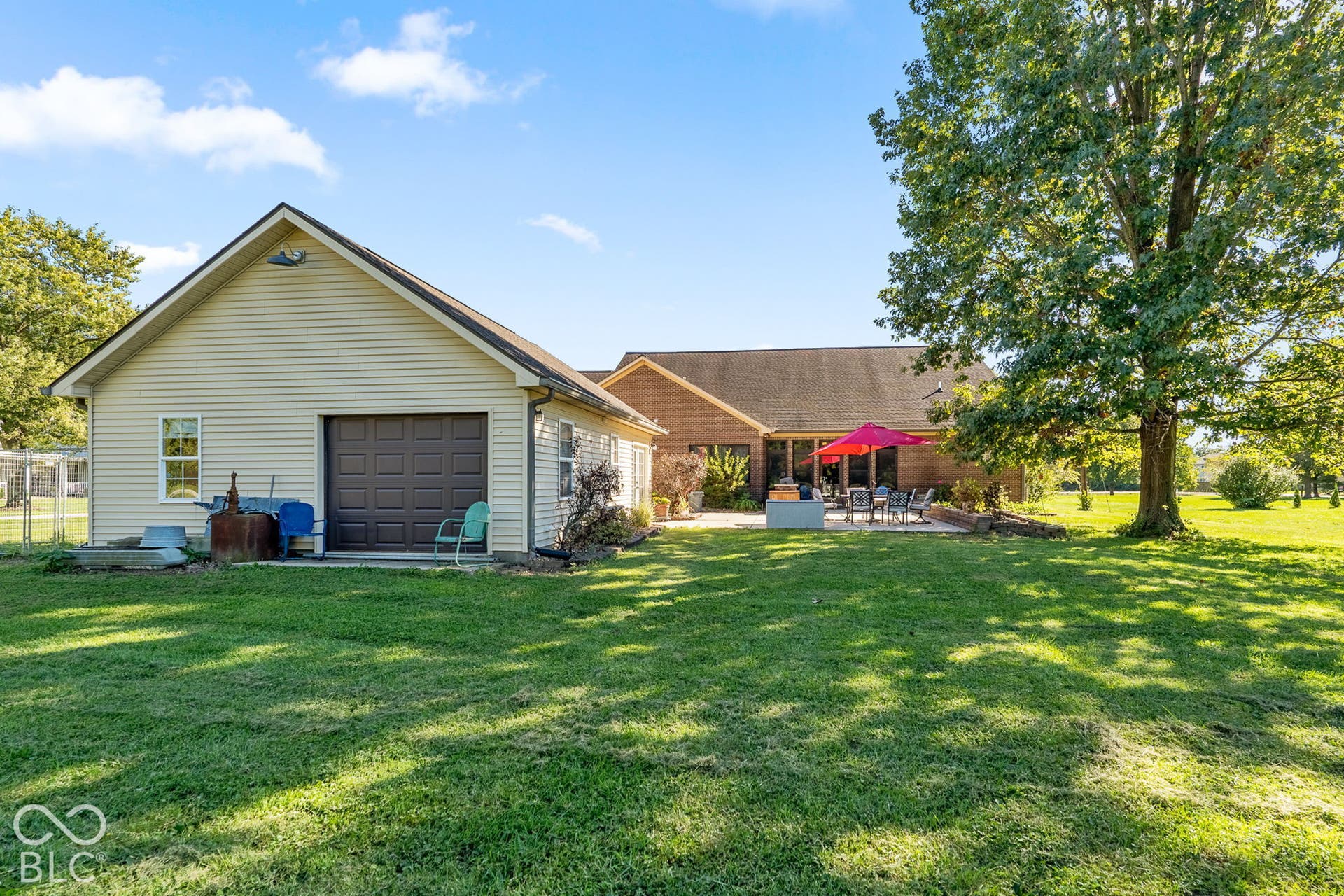 Expansive green lawn, detached garage with siding exterior, paved patio, and mature trees