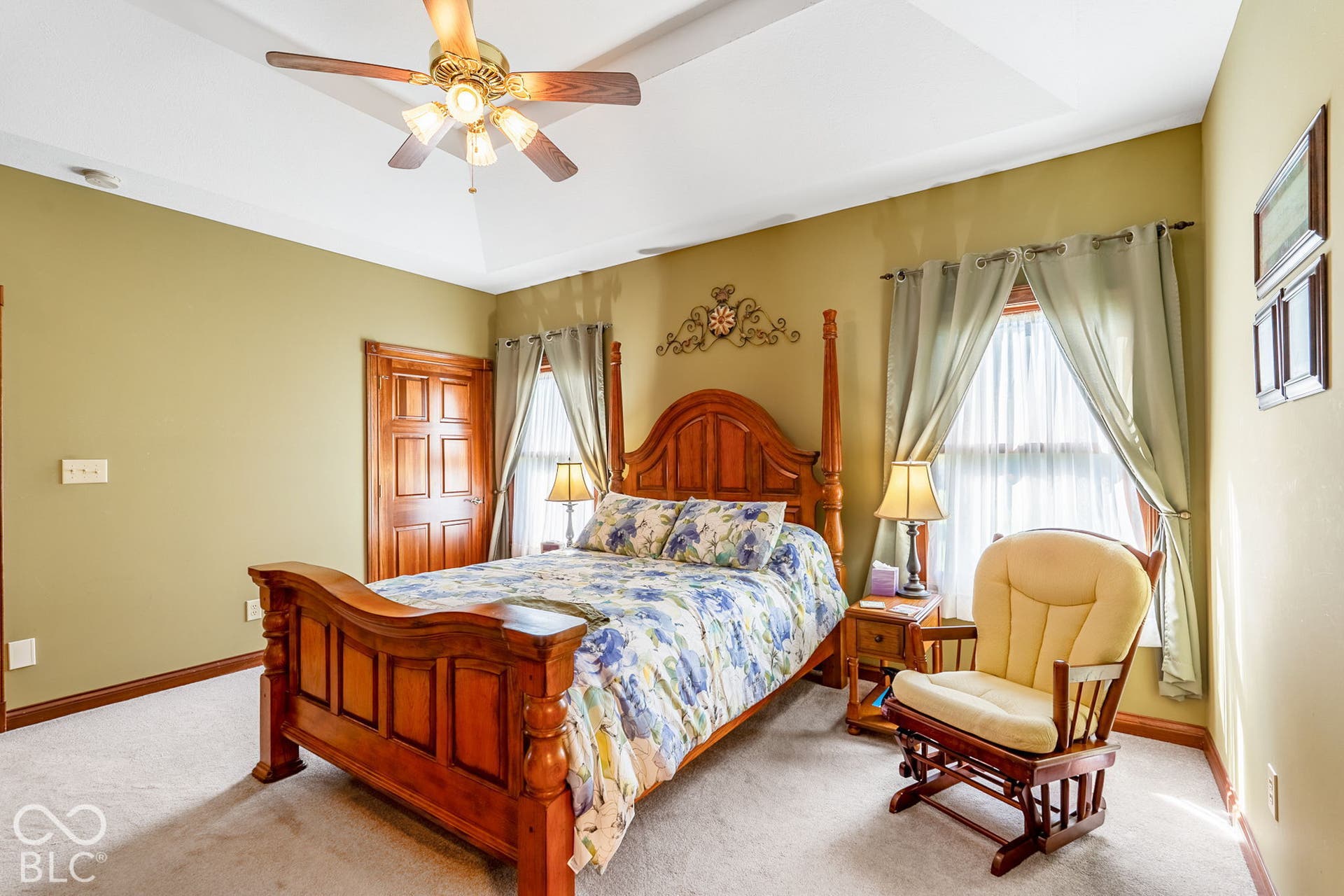 Tray ceiling with a ceiling fan, carpeted flooring, and a paneled wooden door