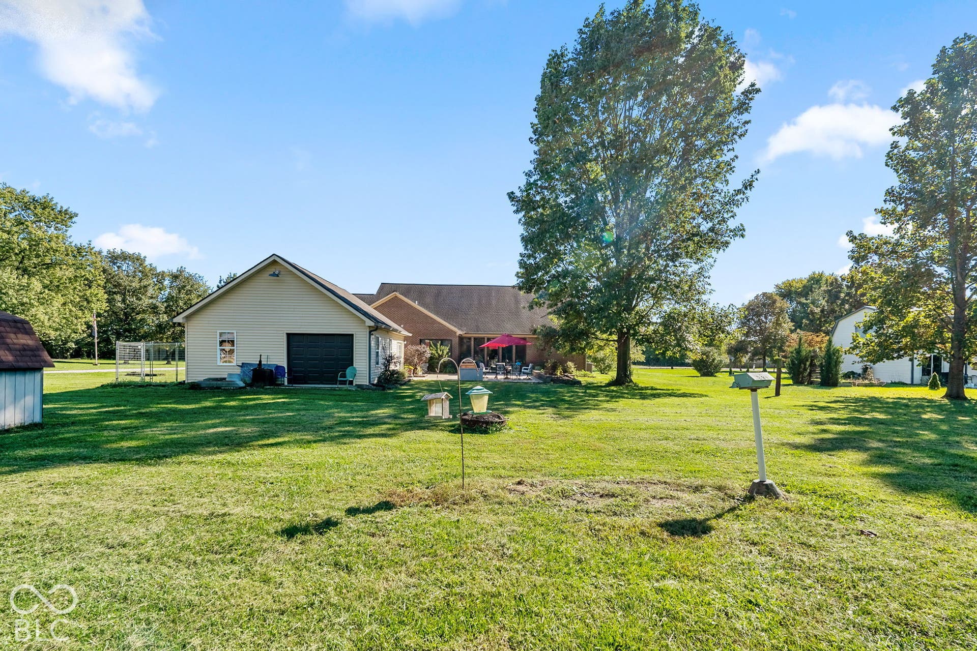 Expansive green lawn with mature trees and a detached structure featuring a garage door