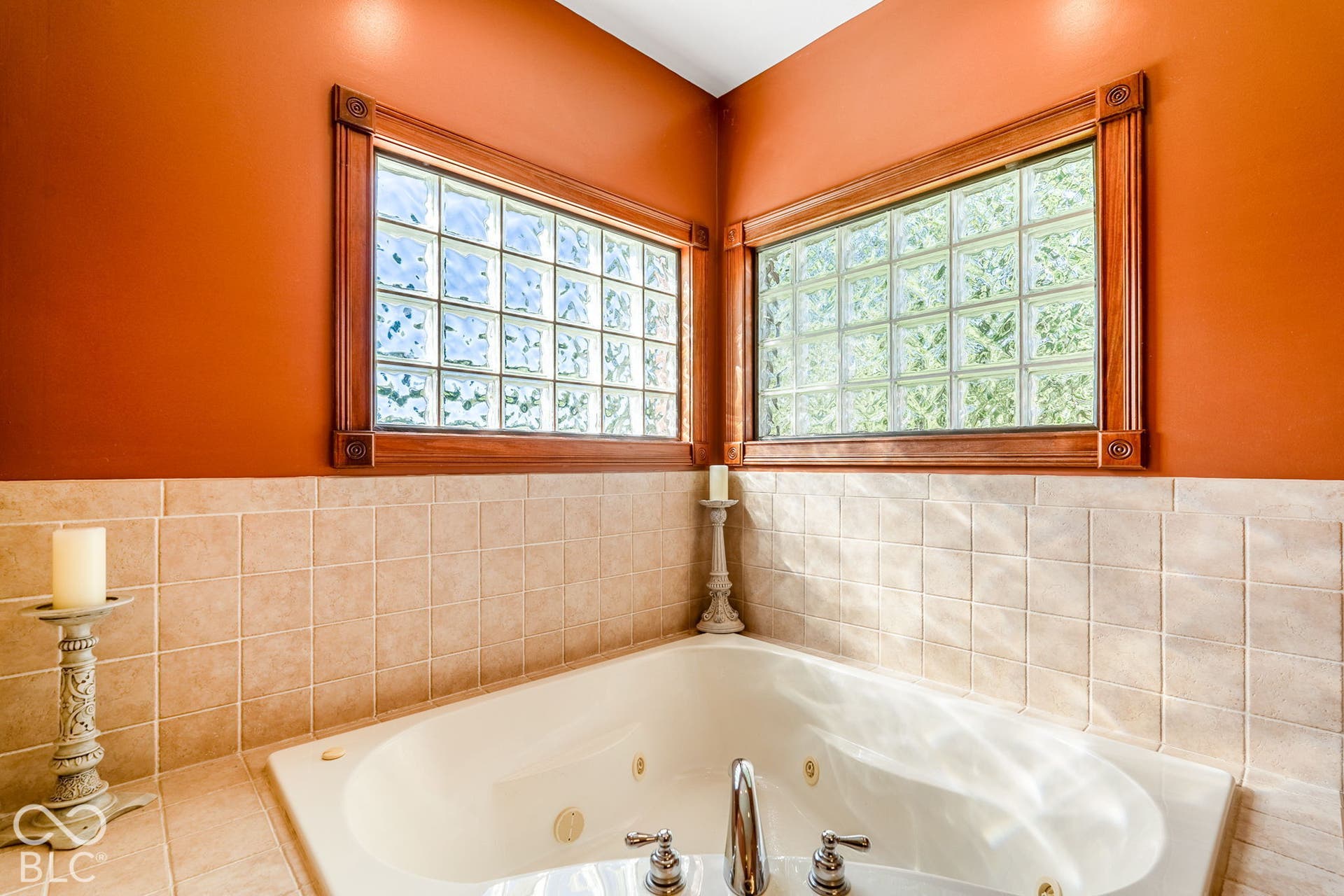 Corner soaking tub with polished chrome fixtures, surrounded by light-toned square tiles