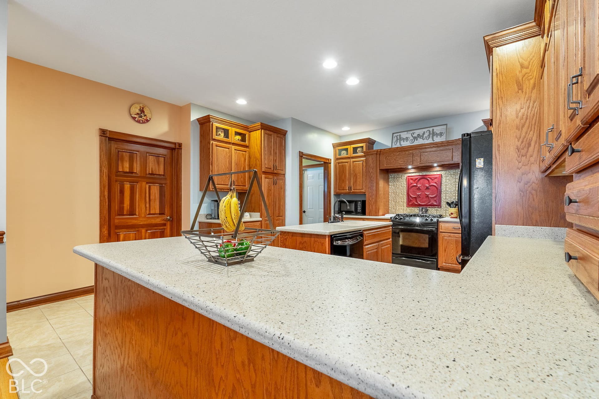 Well-appointed kitchen featuring wood cabinetry, white speckled countertops, a black gas range, and recessed lighting
