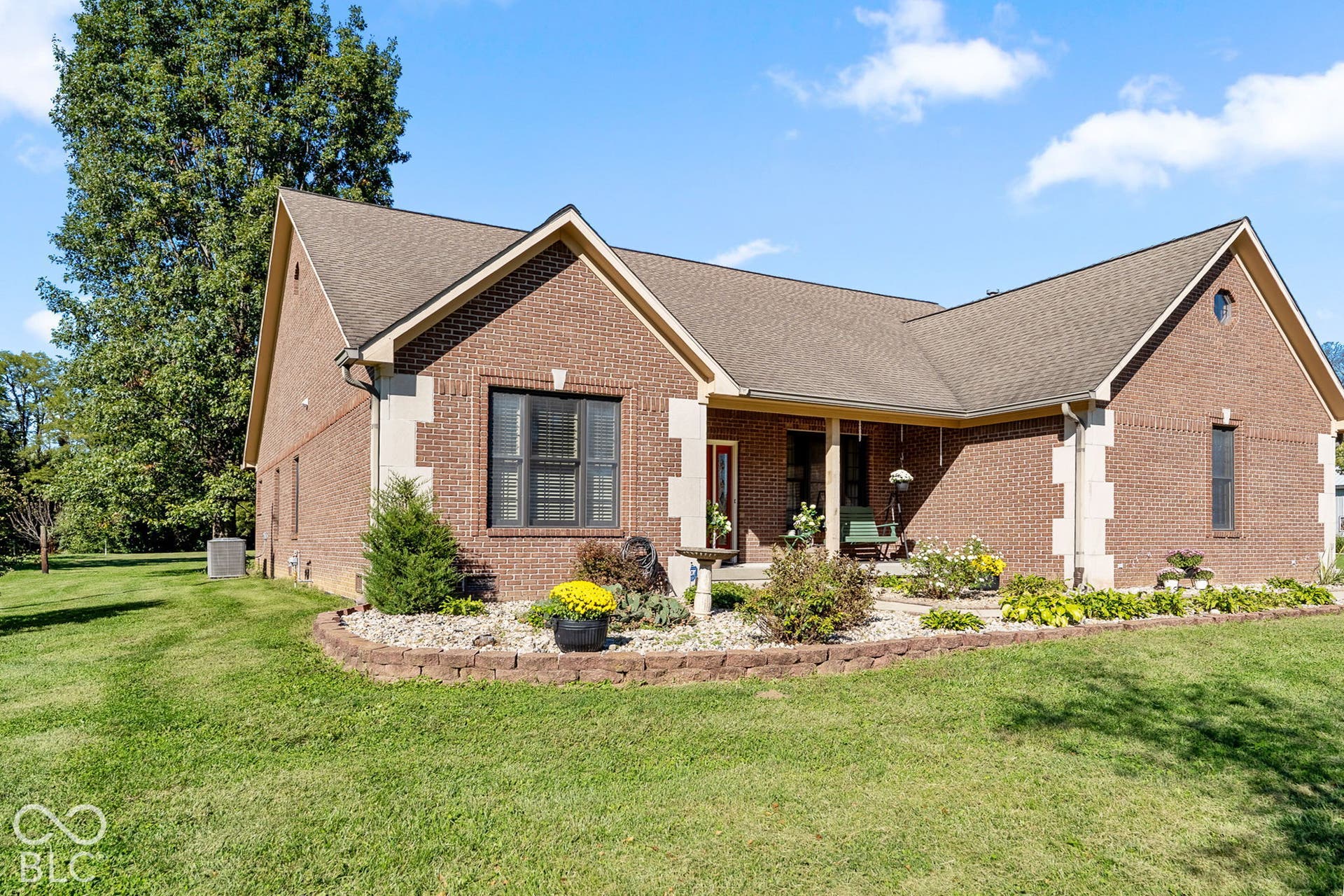 Brick facade with stone accents, covered front porch, gabled rooflines, and a landscaped planting bed