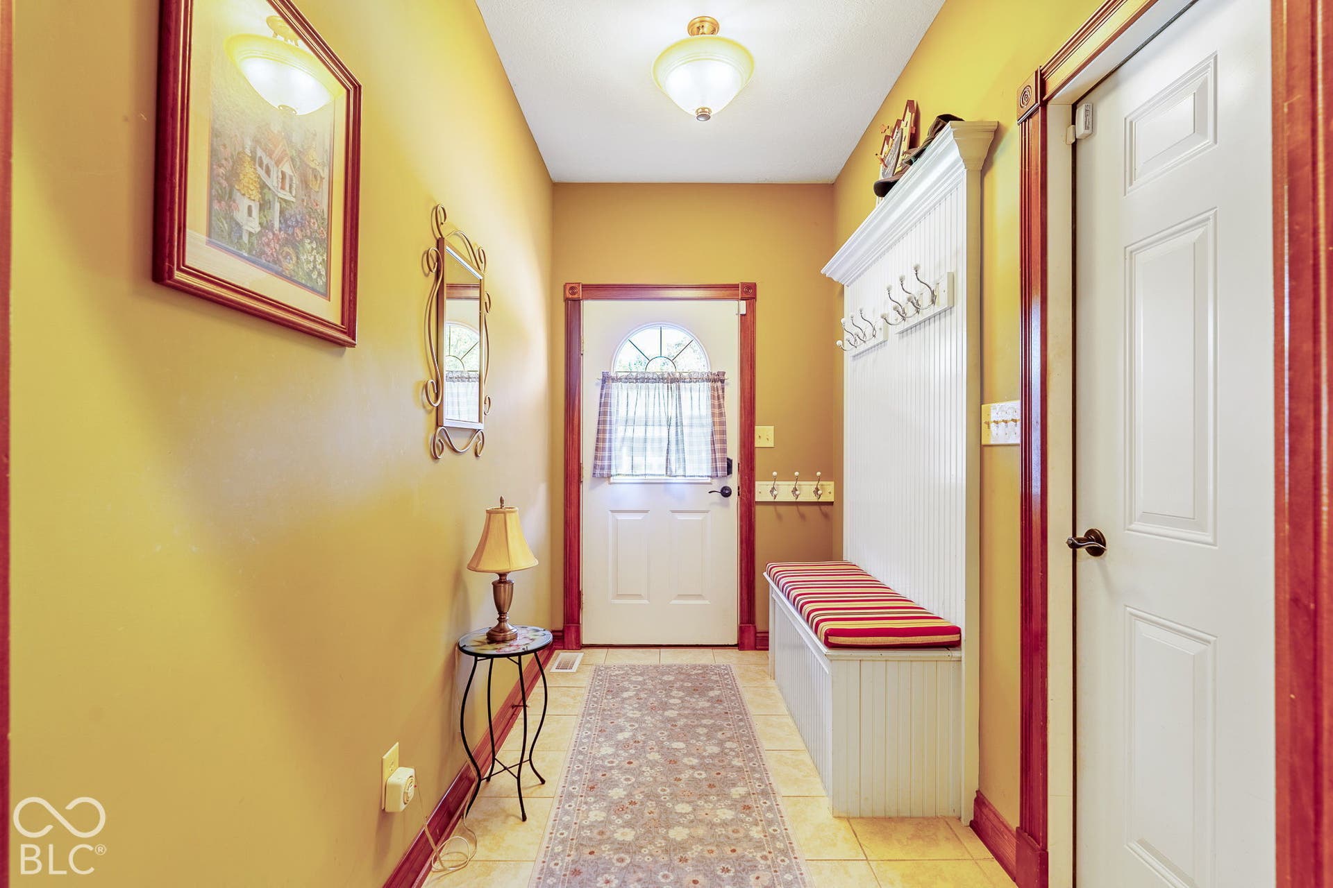 Entryway featuring tile flooring, white paneled accent wall with coat hooks, built-in bench, and a white paneled door with an arched window